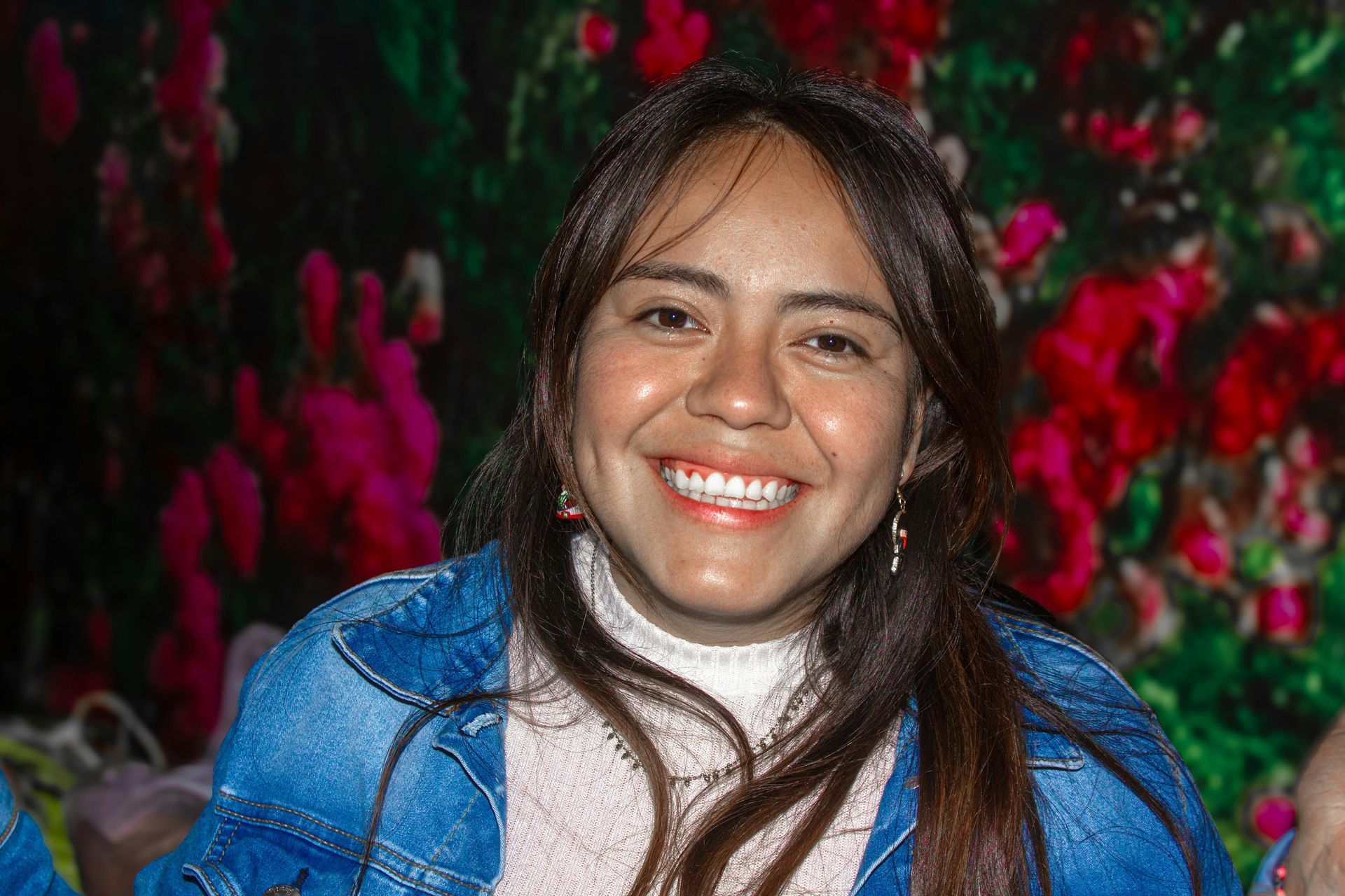 A person rests their chin on their hand at a table decorated with flowers, greenery, and candles against a brick wall.