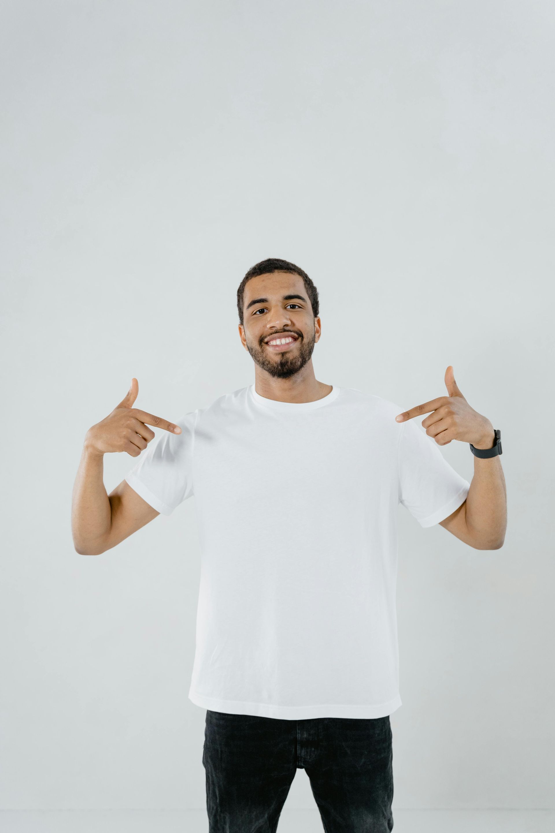 A person with dark, curly hair wearing glasses and a yellow t-shirt, smiling against a plain light gray background.