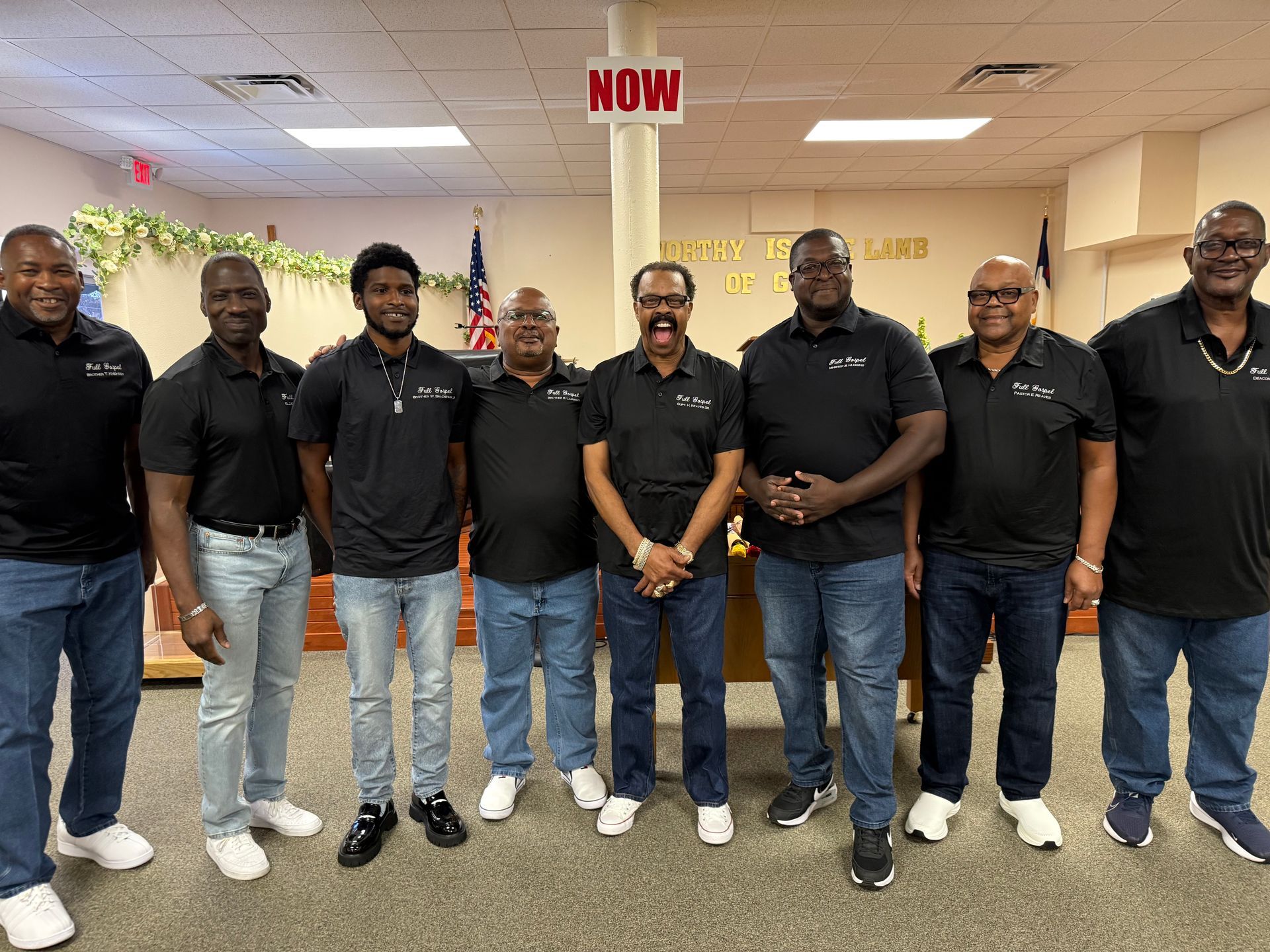 Group of men in black shirts and jeans, posing indoors.