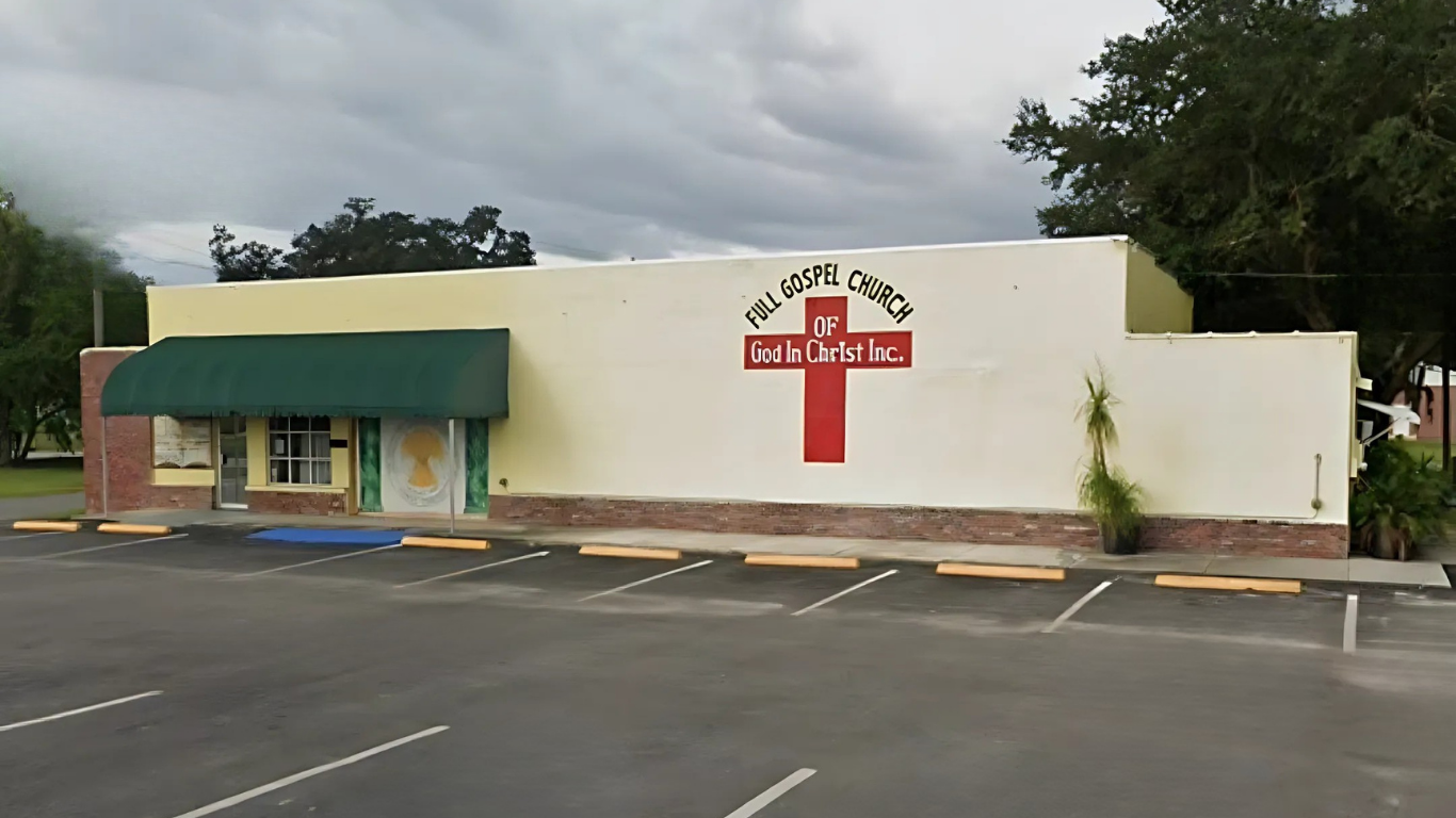 Exterior of Full Hope Church with a red cross on the wall. Includes an awning, trees, and parking.