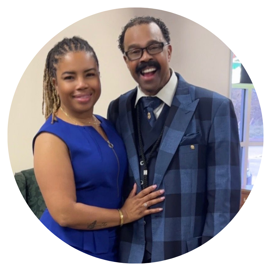 Woman in blue dress and man in checkered suit smile together indoors.