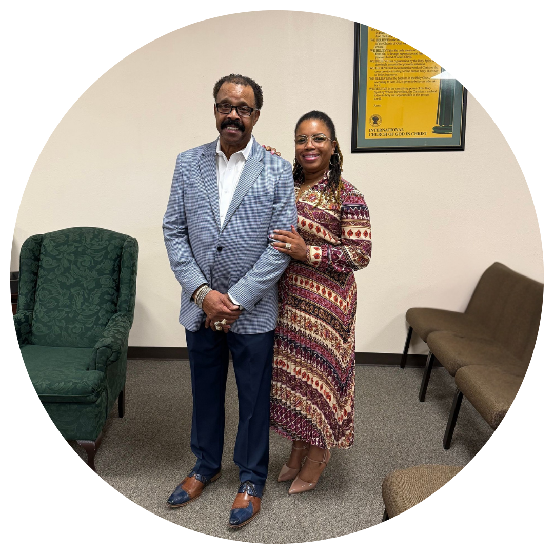Woman in blue dress and man in checkered suit smile together indoors.