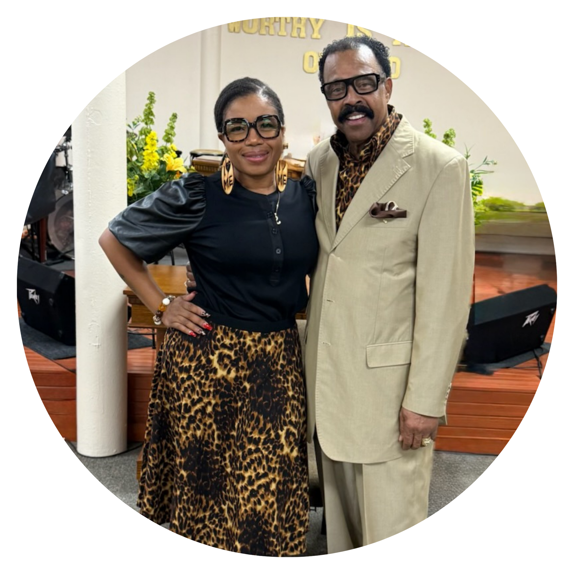 Woman in blue dress and man in checkered suit smile together indoors.