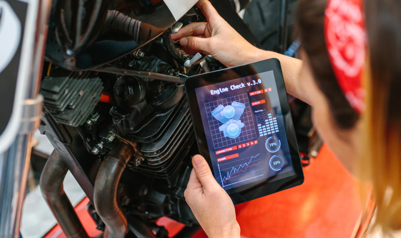 A person is holding a tablet in front of a motorcycle engine.