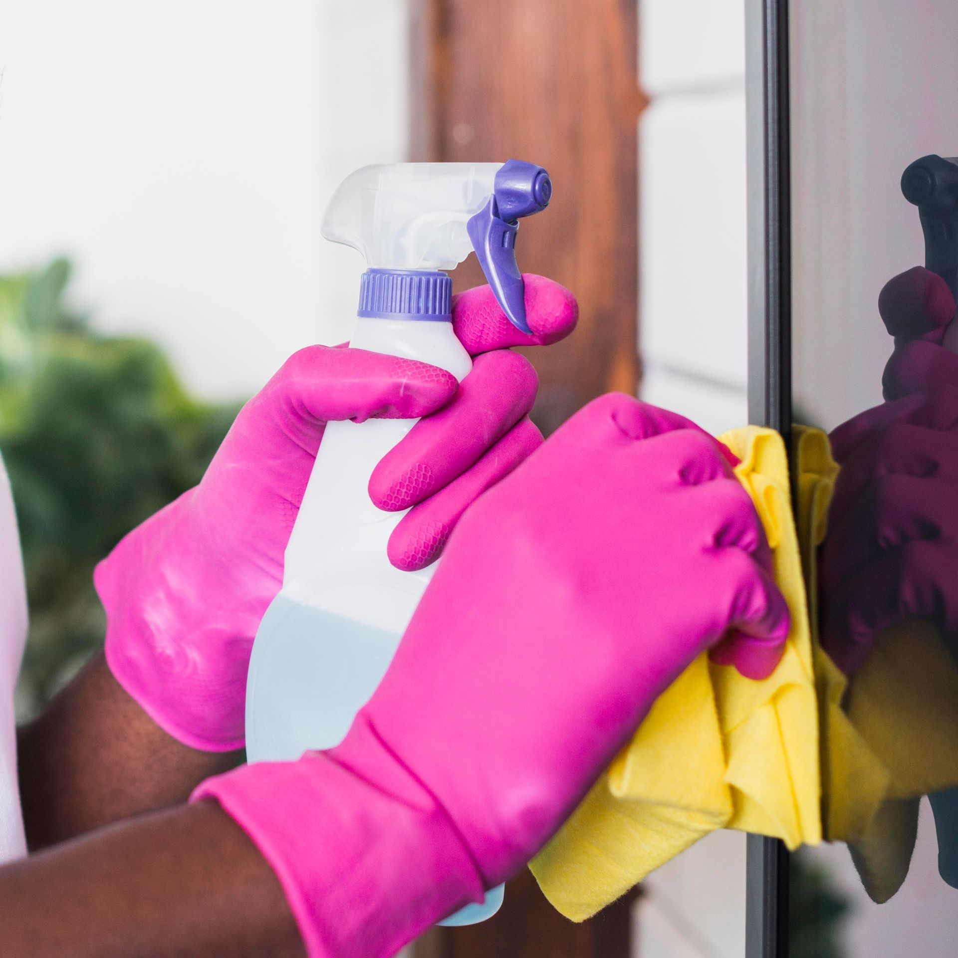 Person wearing pink gloves sprays cleaner and wipes a dark surface with a yellow cloth.