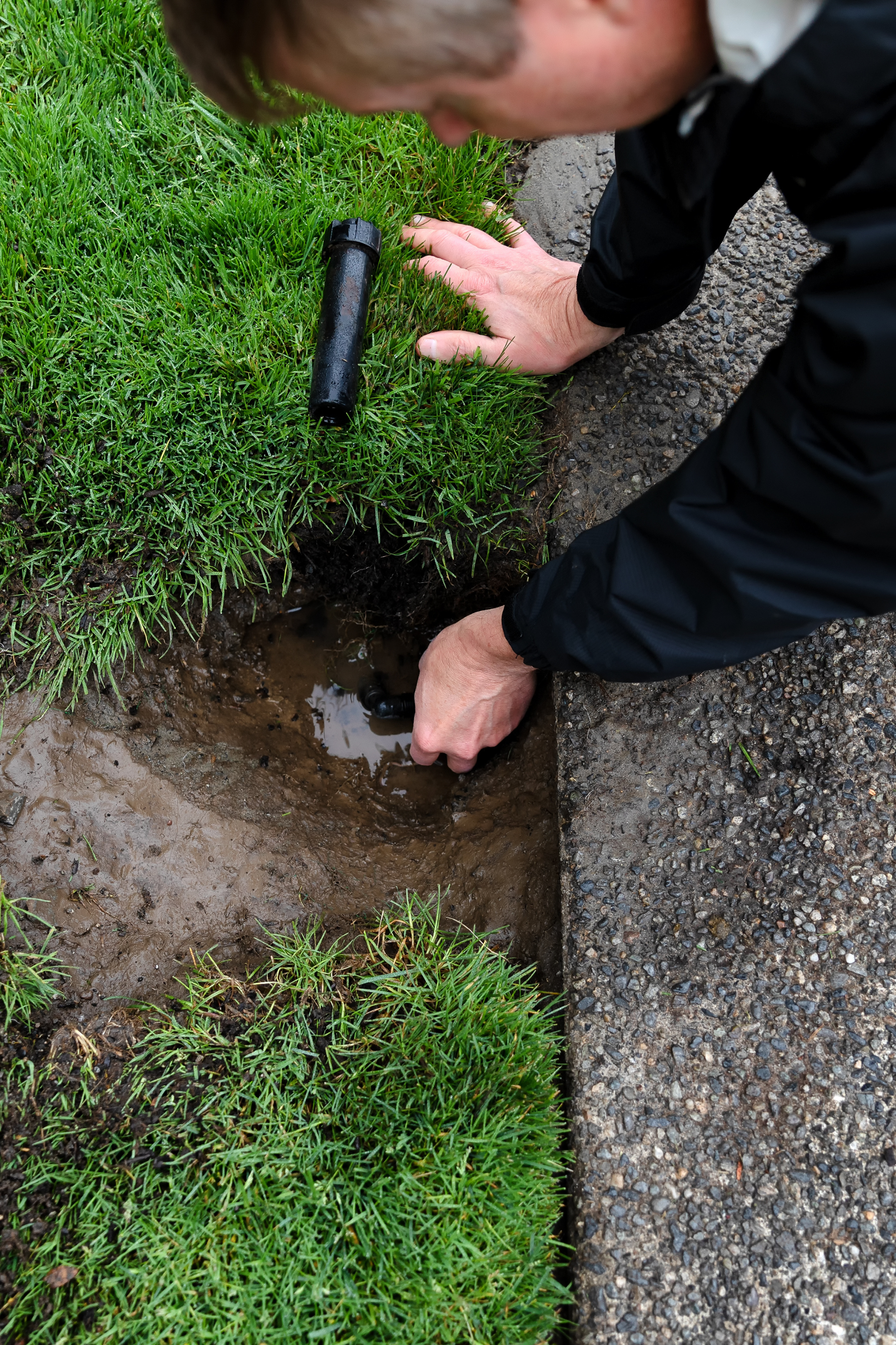 A man is looking at a sprinkler in the grass.