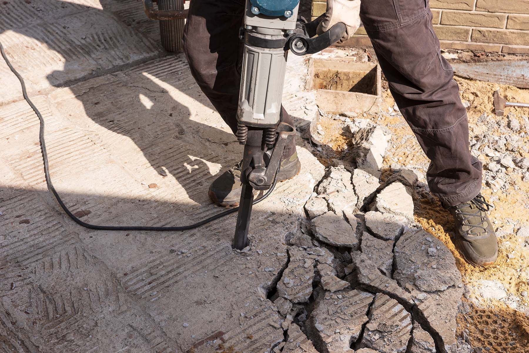 Ein Mann benutzt einen Hammer, um Beton zu zerschlagen.