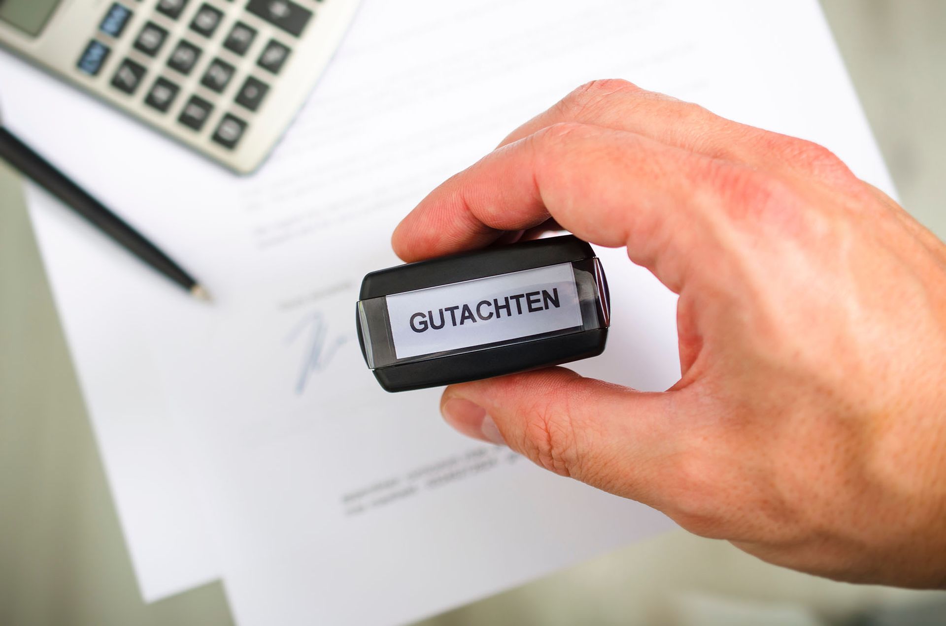 Eine Person hält einen Stempel mit der Aufschrift „Gutachten“ in der Hand.