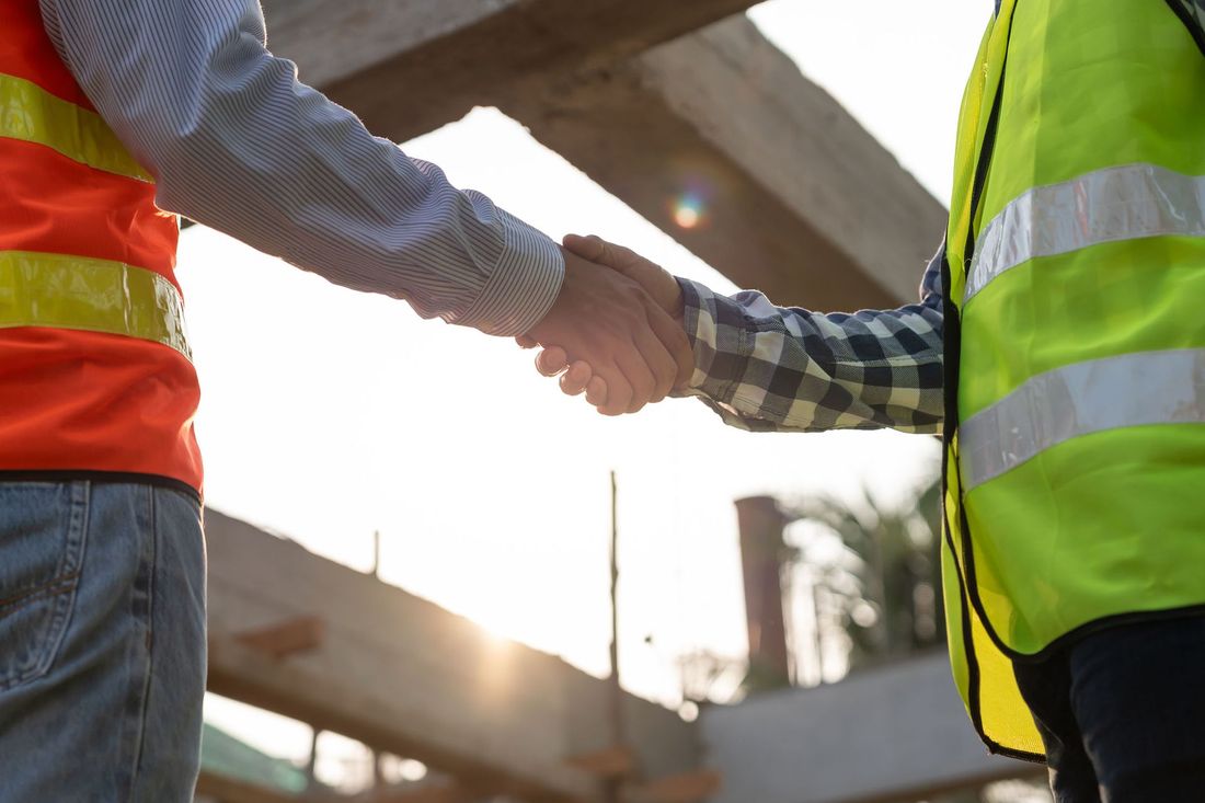 Zwei Bauarbeiter geben sich auf einer Baustelle die Hand.