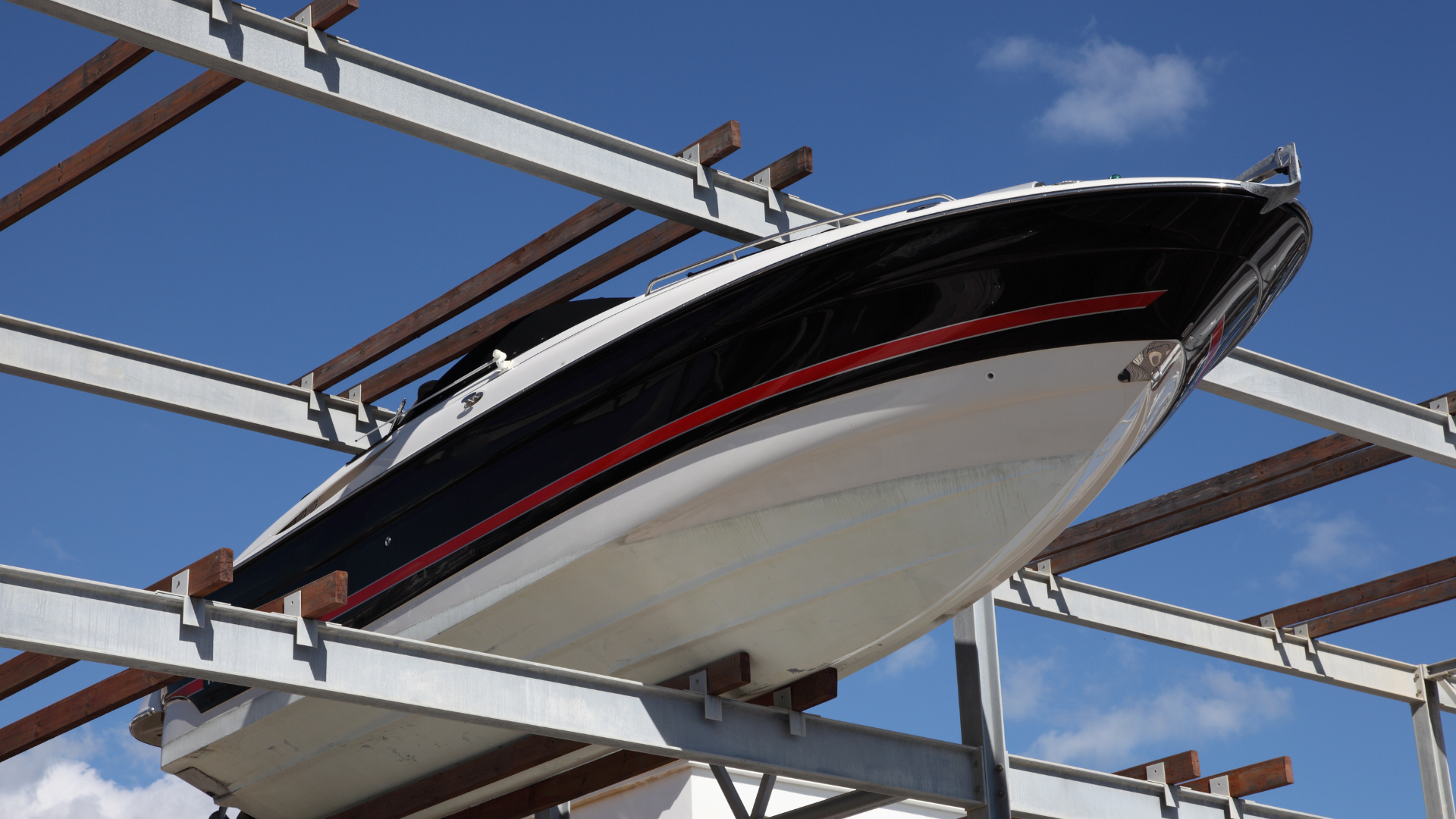 Boat in black, red and white on a rack under a blue sky.