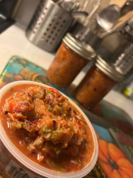 Close-up of salsa in a container with two jars in the background, all on a colorful placemat.