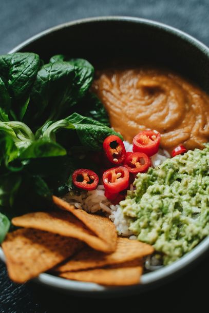 A close up of a bowl of food with guacamole , tortilla chips , spinach and peppers.