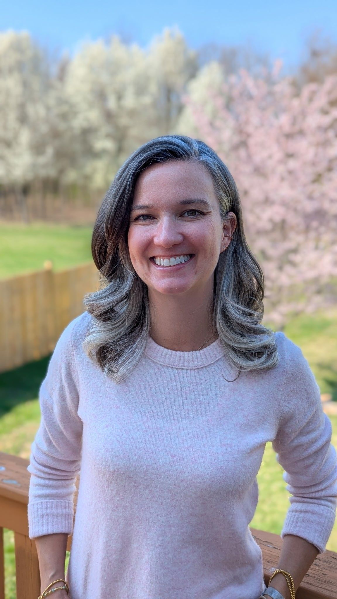 Woman in sweater smiles, wearing a white shirt outside.