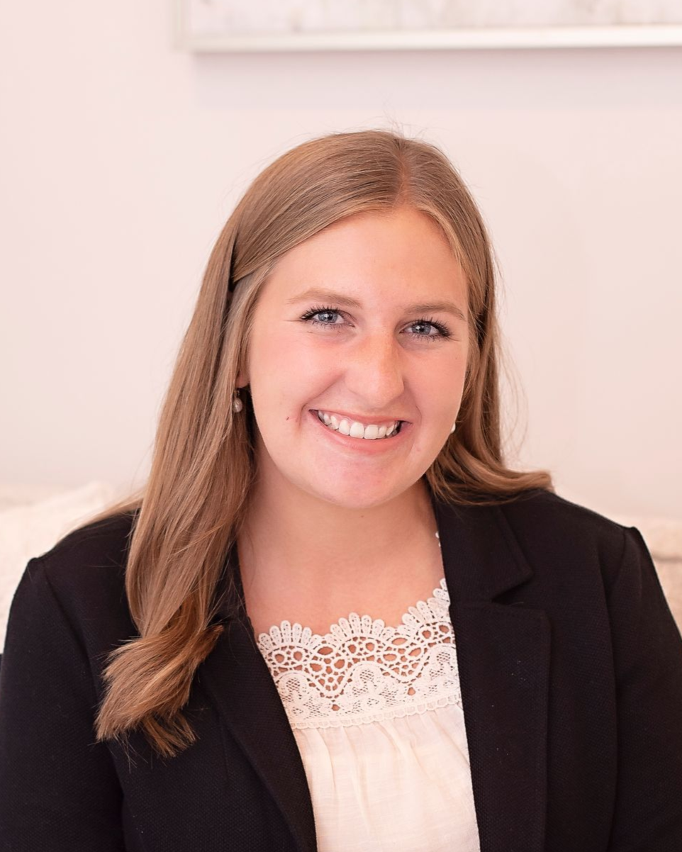 Woman with long blonde hair, smiling, wearing a black blazer and white top.