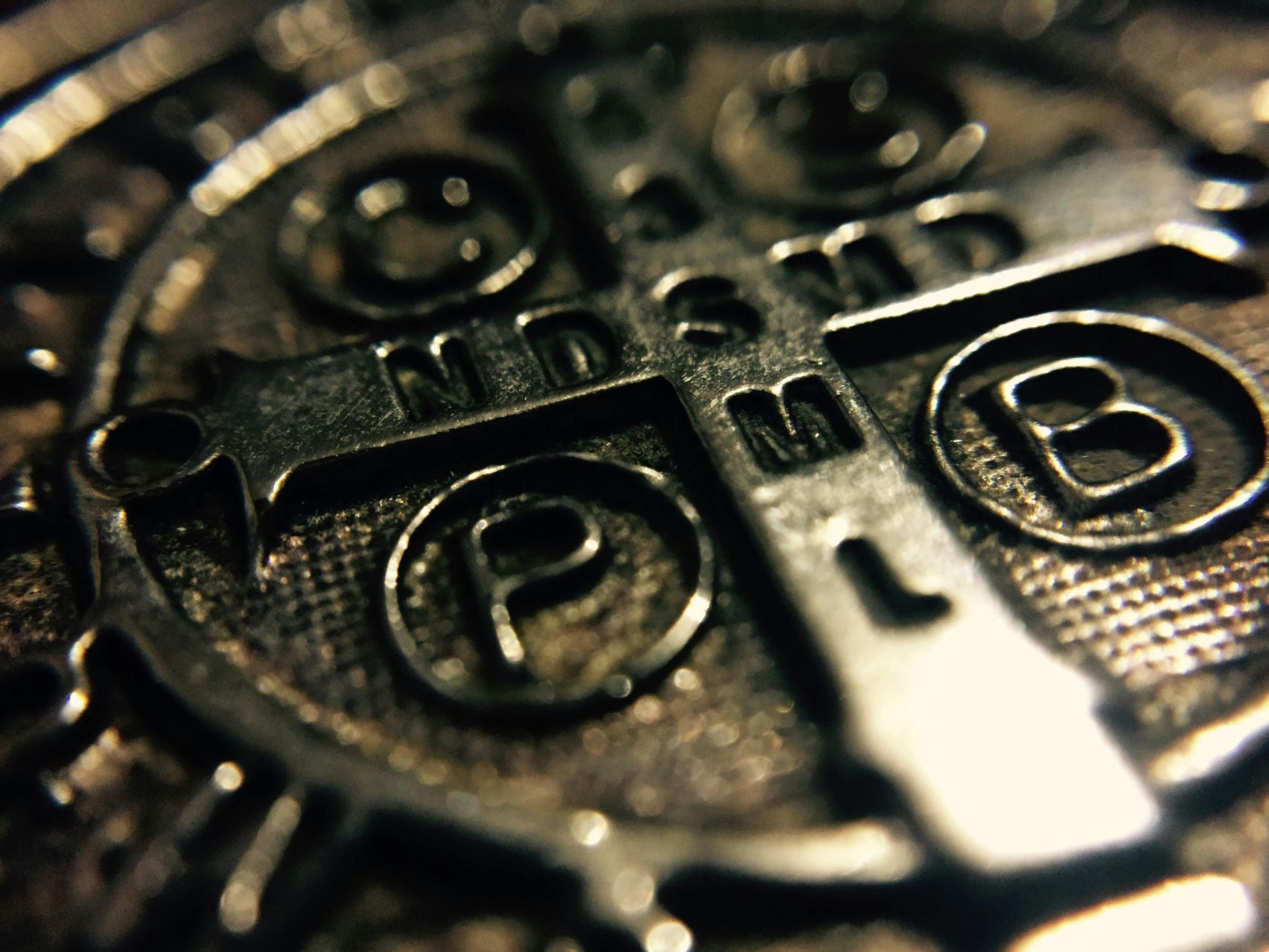 Close-up of a silver St. Benedict medal with religious inscriptions, including a cross and circular letters.