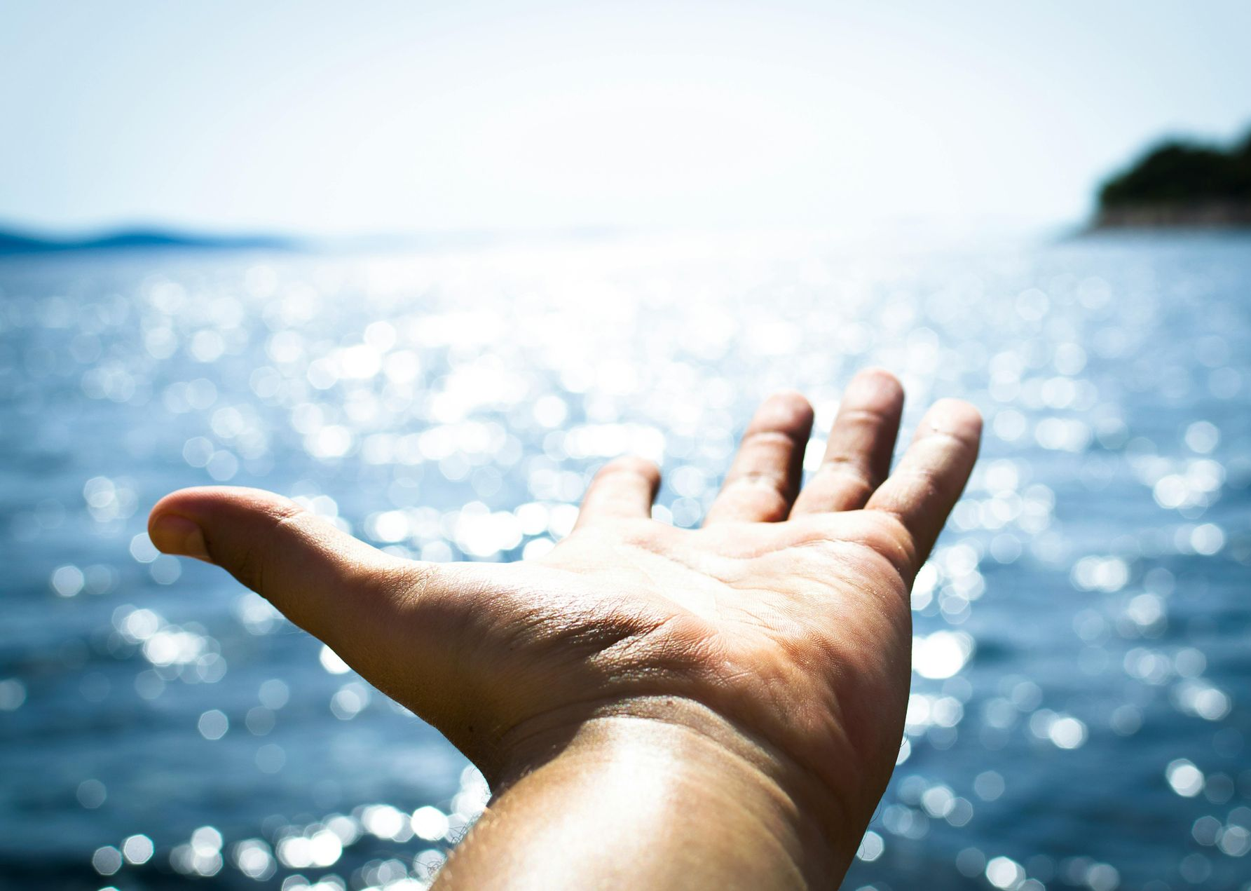 Open hand with palm up against a bright, shimmering ocean backdrop.