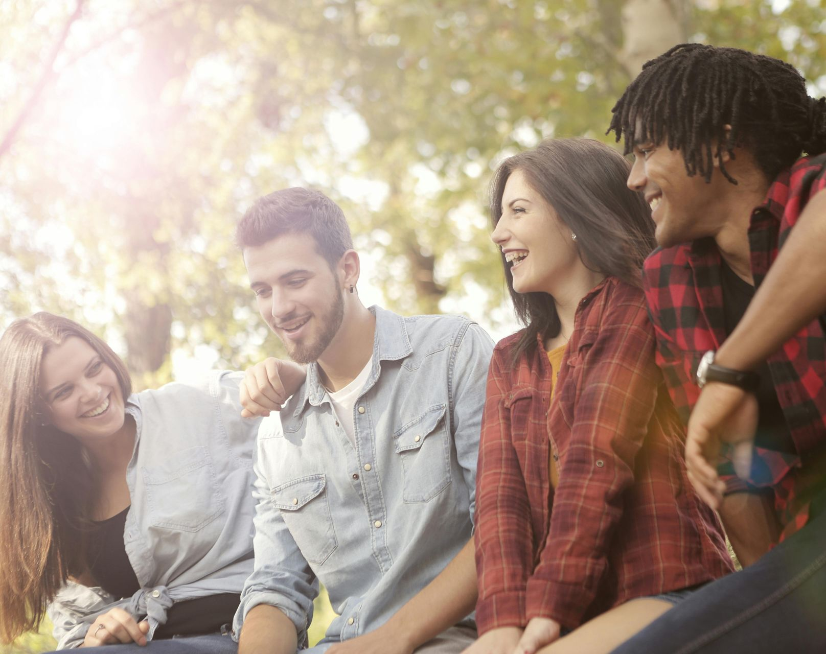 Four young adults laughing outdoors, bathed in sunlight.