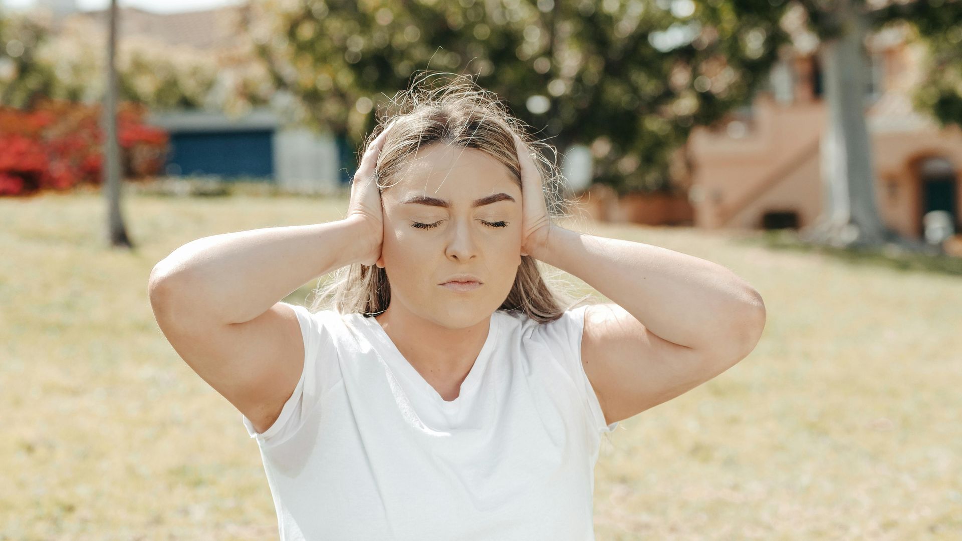 Woman with closed eyes covering ears outside.