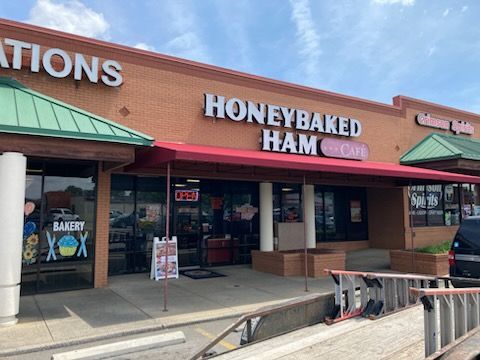 The front of a honeybaked ham restaurant with a red awning.