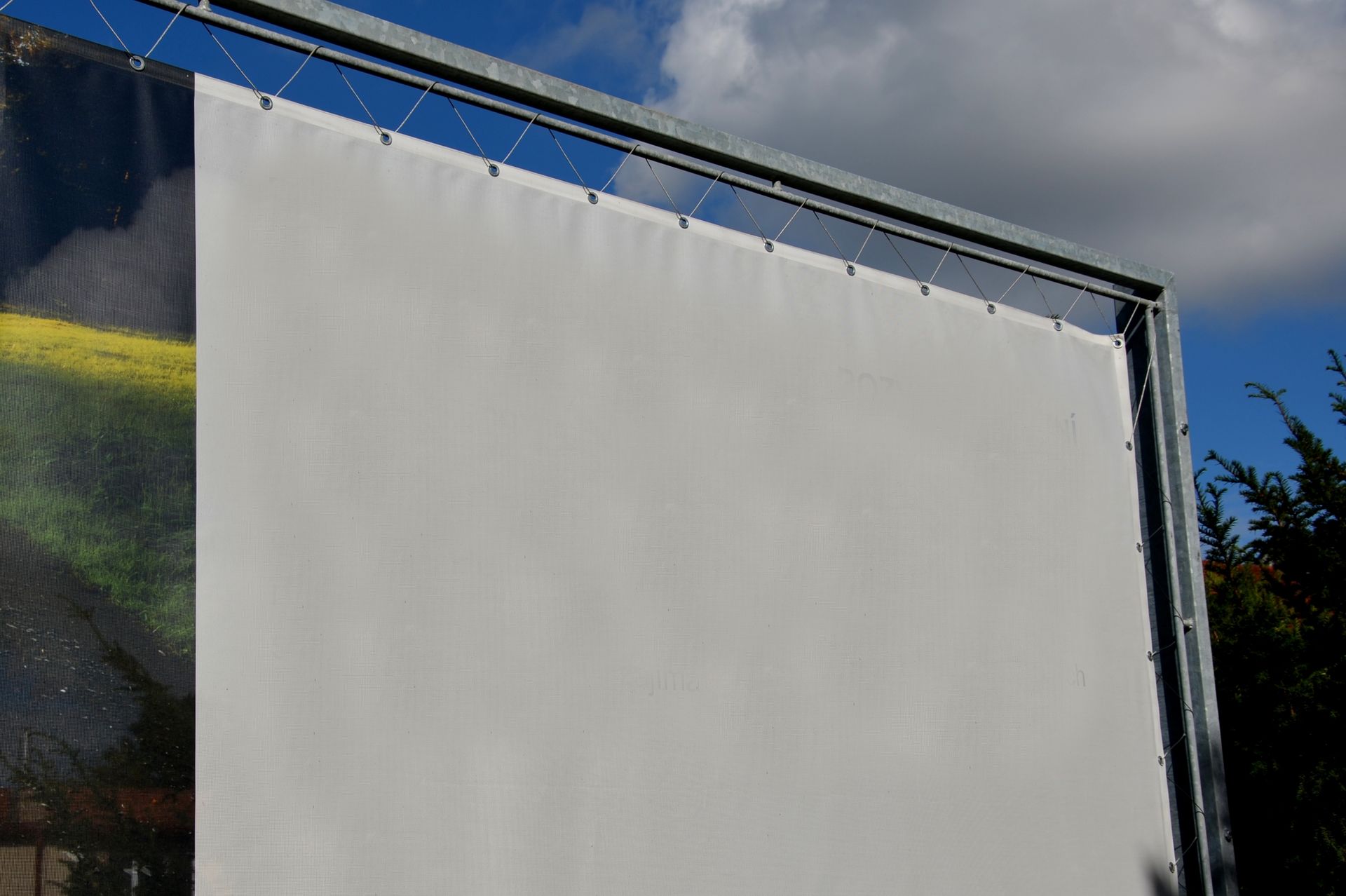 A large white billboard is attached to a metal fence.
