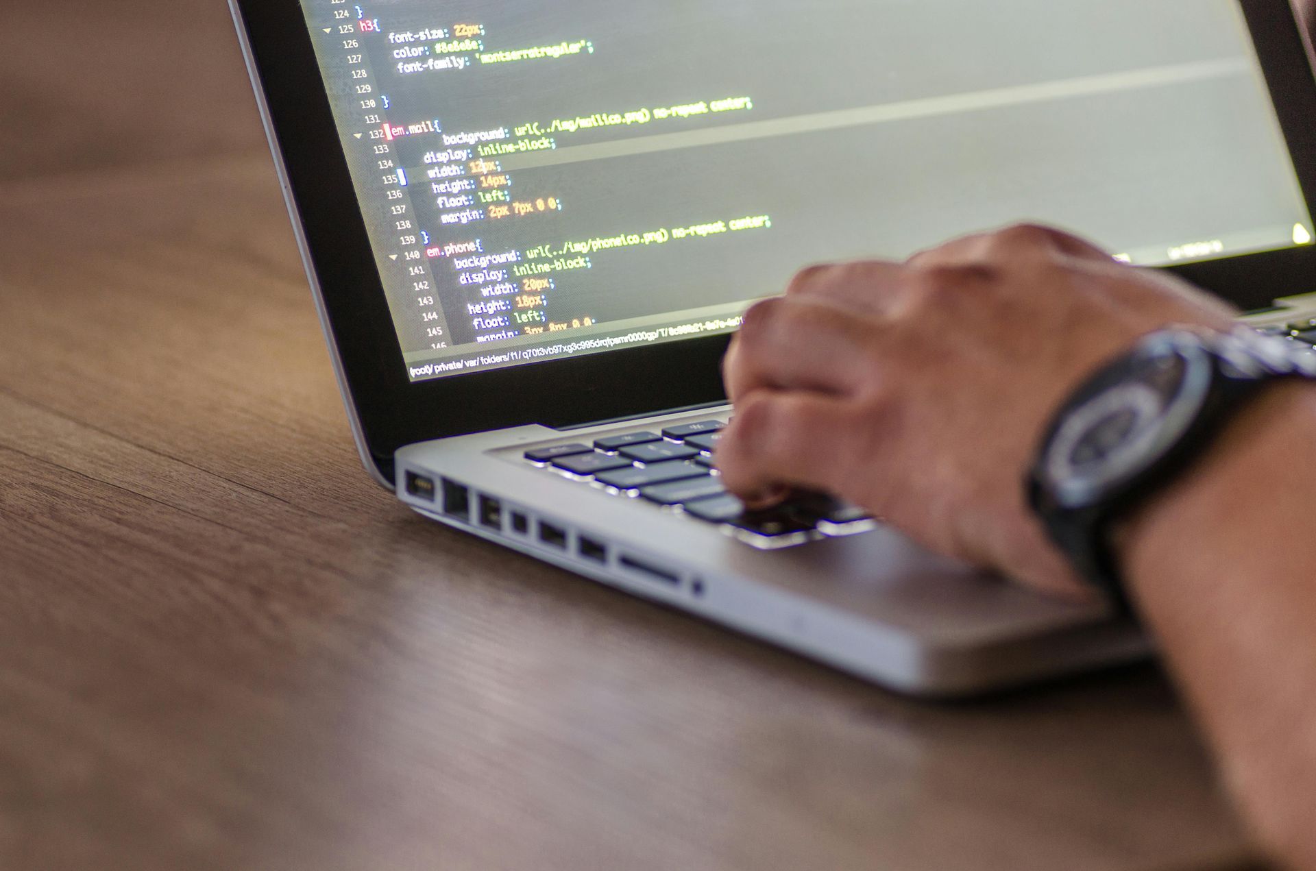 A person wearing a watch is typing on a laptop computer.