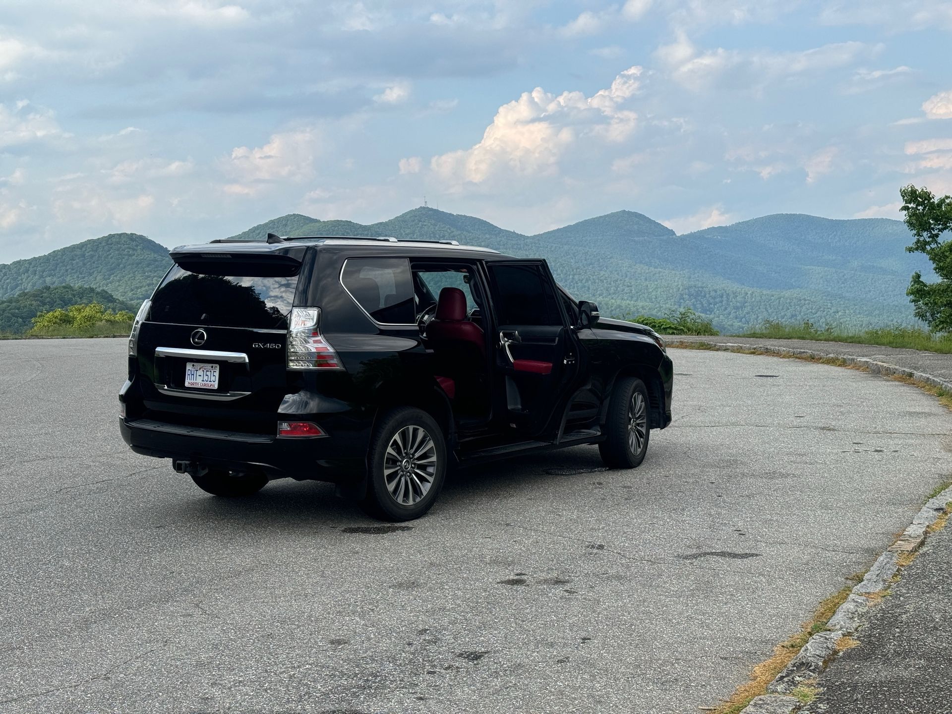 Black SUV parked on a road with a mountain backdrop. Open driver's side door reveals red interior.