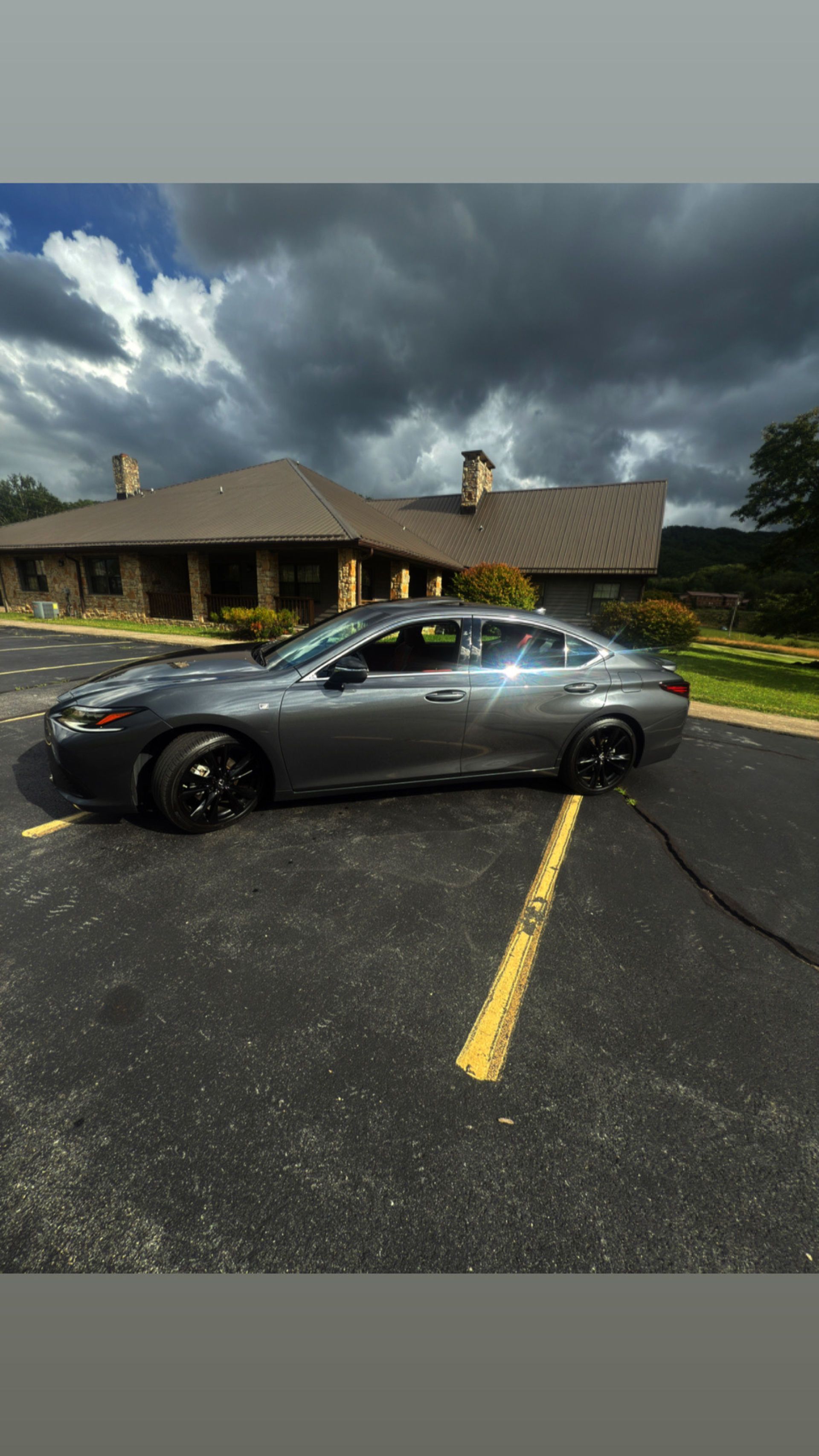 Gray car parked on asphalt in front of a building with a dark sky overhead.