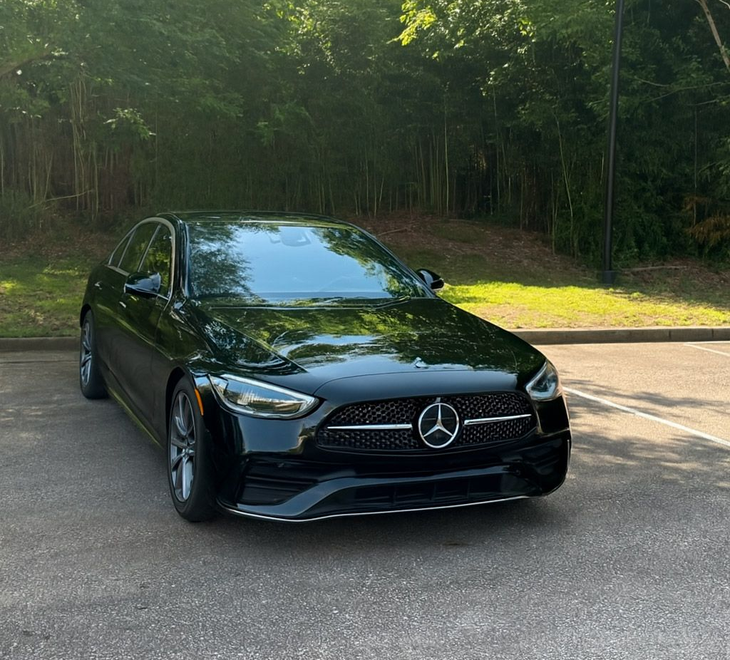 Black Mercedes-Benz sedan parked on pavement, in front of trees.