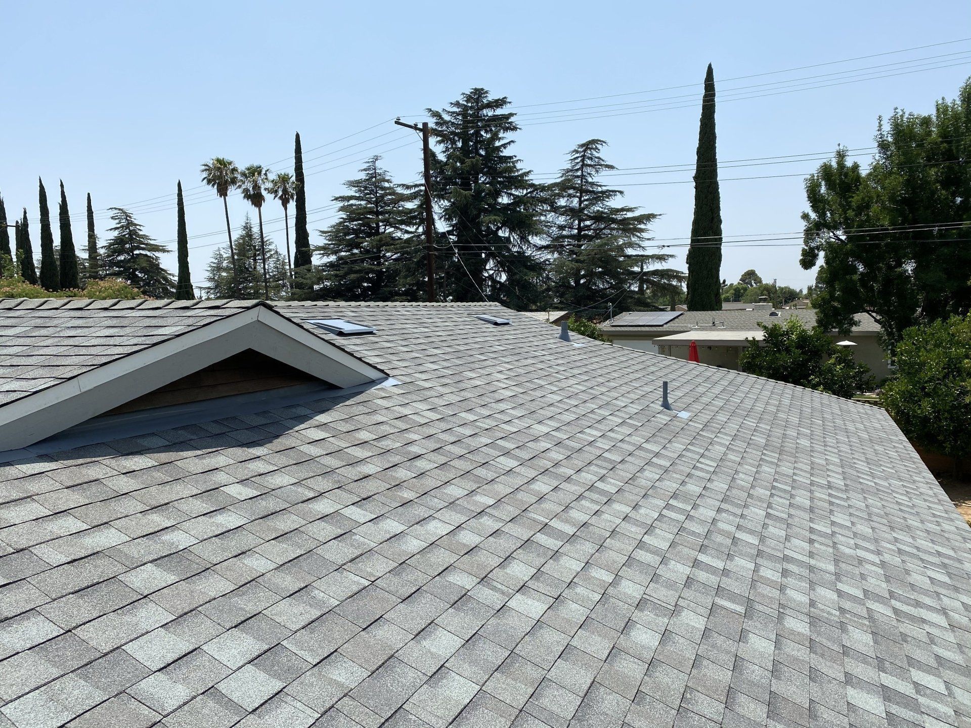 Gray shingle roof with a small vent and gabled roof with trees and blue sky