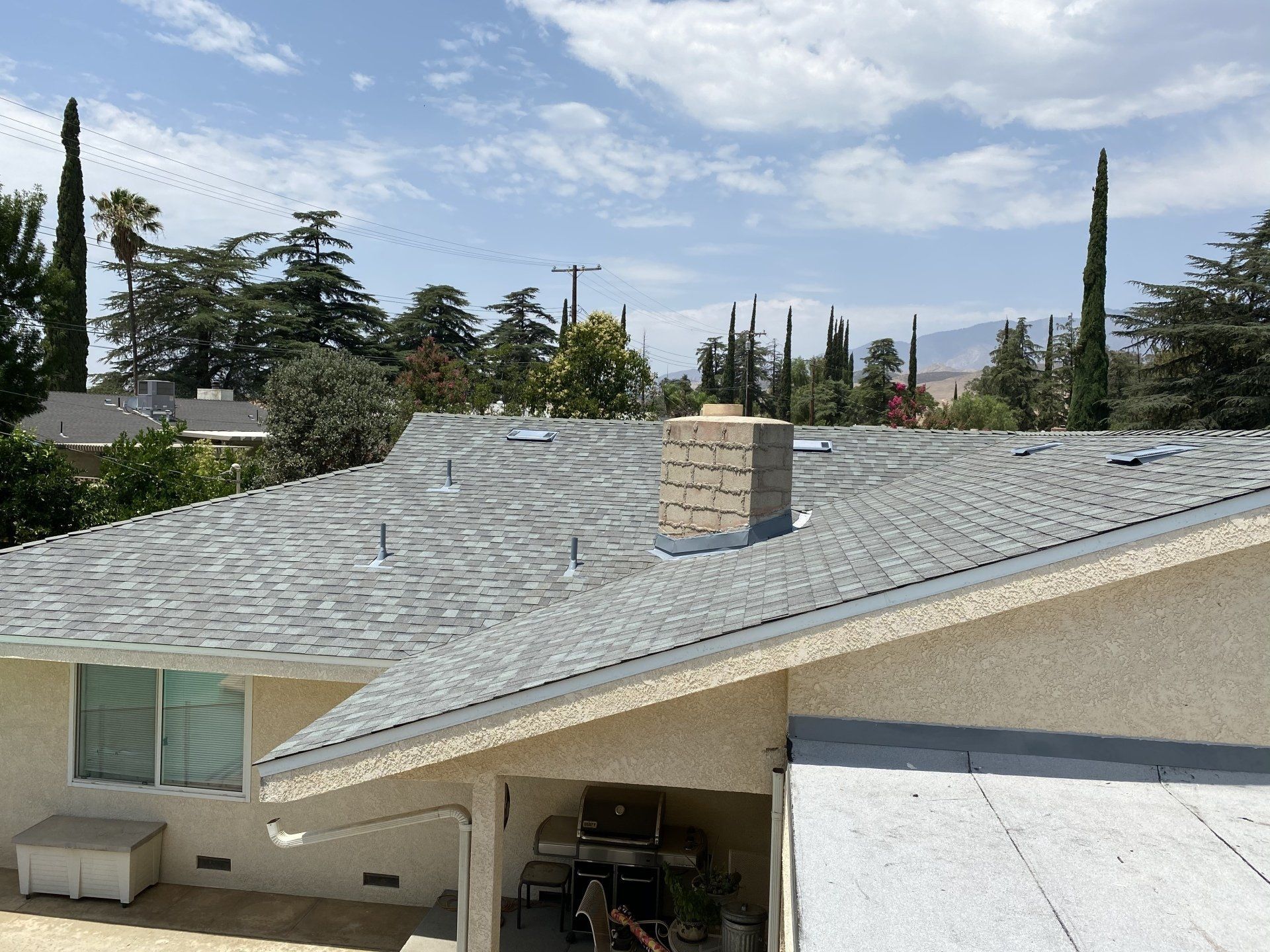 A light-colored house with a new gray shingle roof, chimney, and a view of trees and mountains
