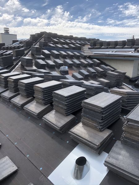 Rooftop with stacks of dark tiles ready for installation, against a cloudy sky