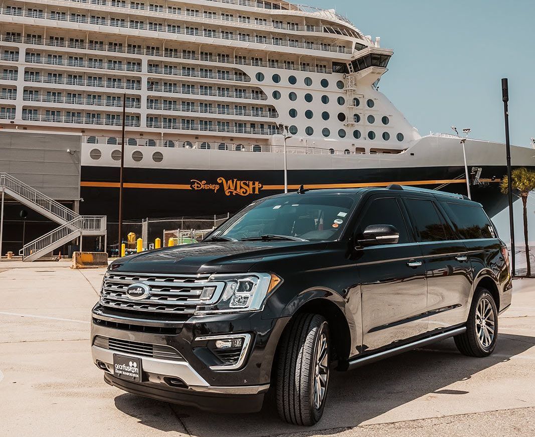 A black suv is parked in front of a cruise ship.