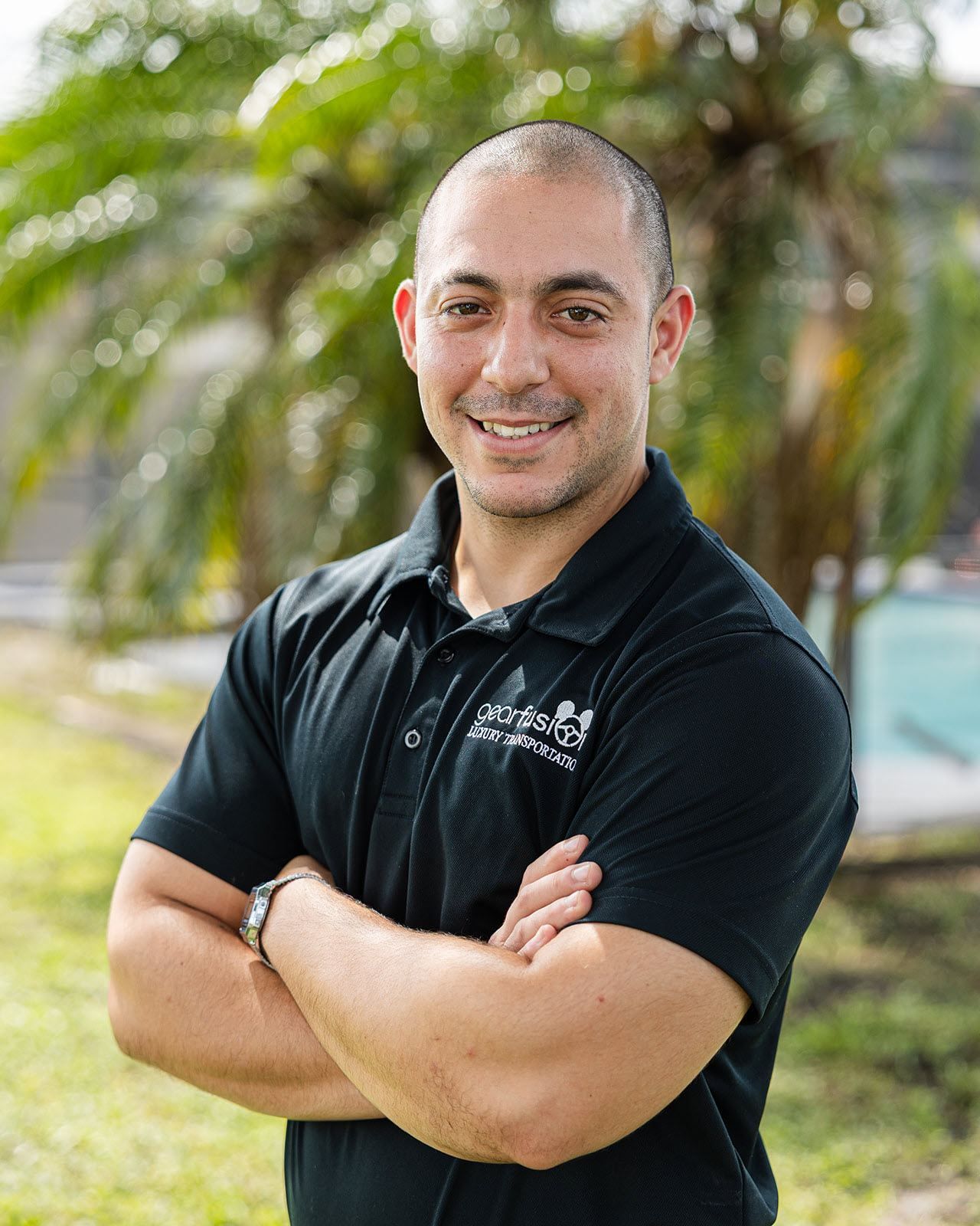 A man in a black shirt is standing with his arms crossed and smiling.