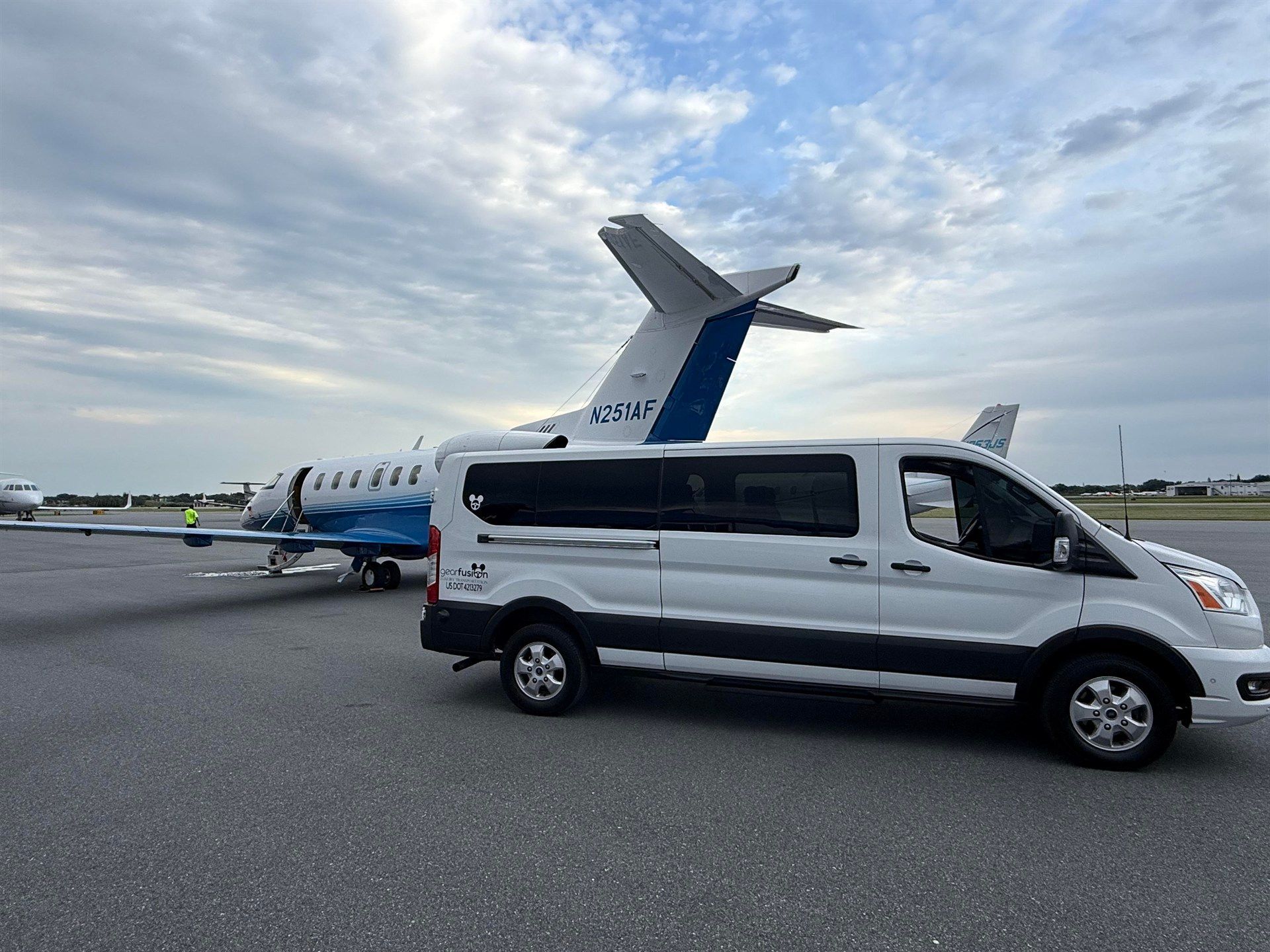 A white van is parked next to an airplane on a runway.