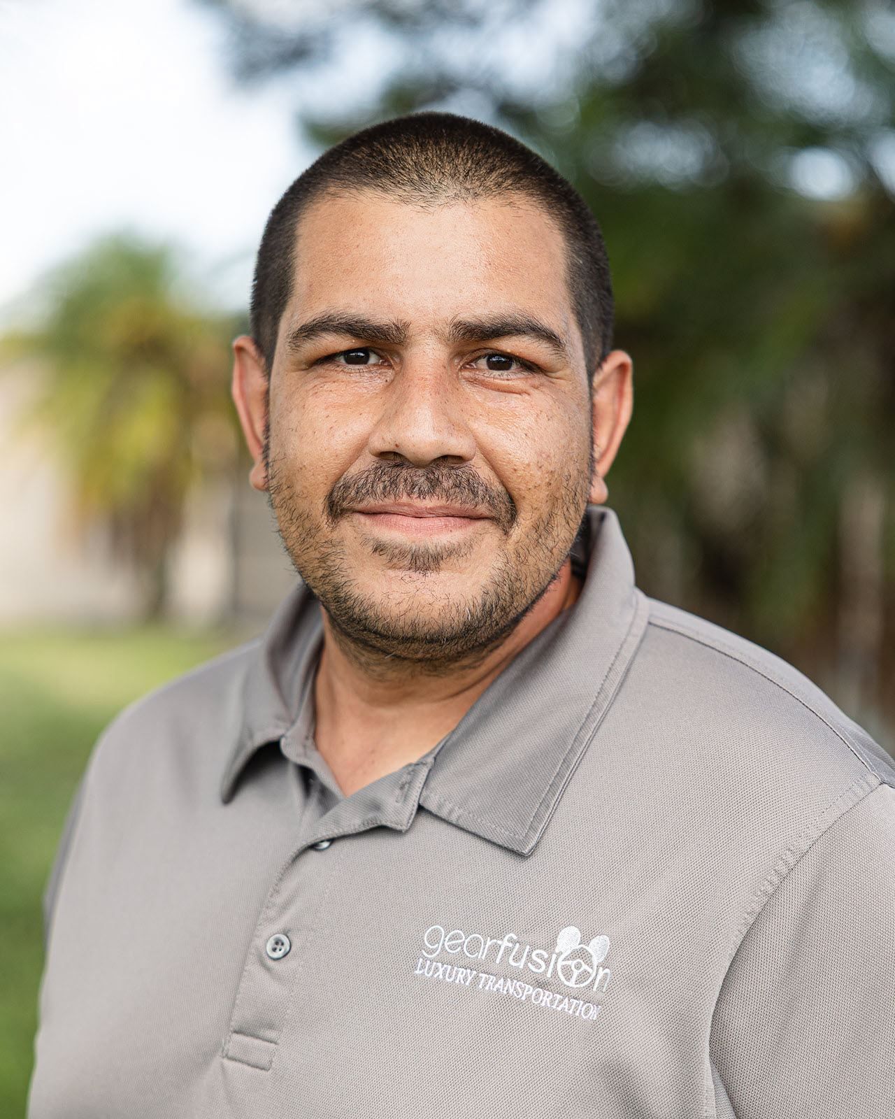 A man with a beard is wearing a gray shirt and smiling for the camera.