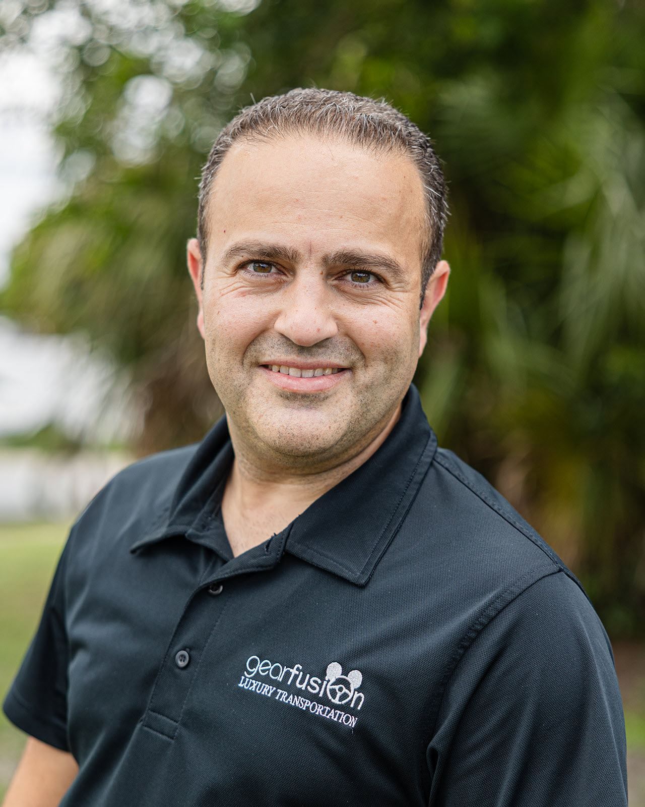 A man in a black shirt is standing in front of a tree.