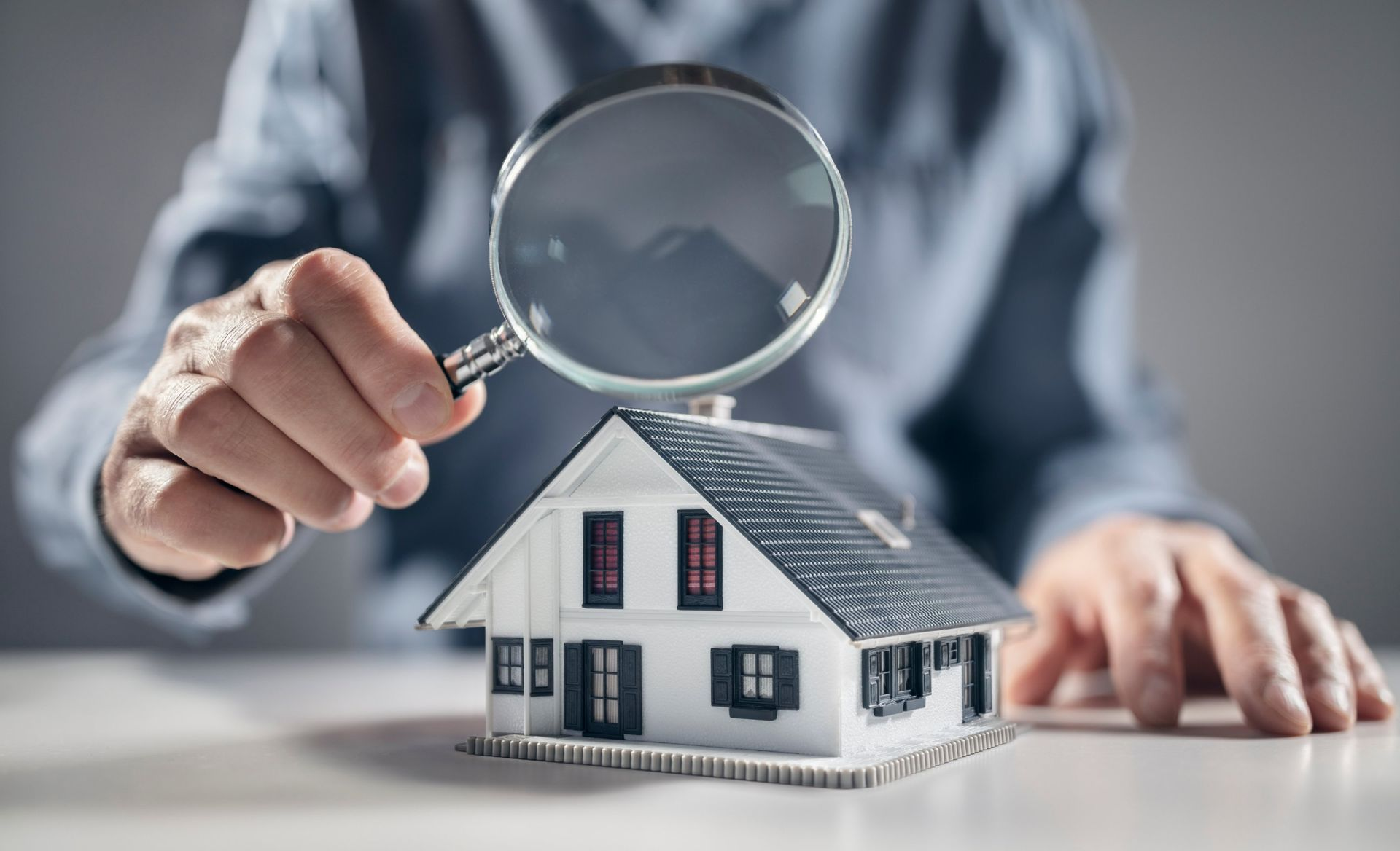 Person with magnifying glass inspecting a model house on a table.