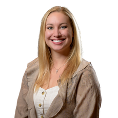 Blonde woman with a genuine smile wearing a light brown jacket and white top, looking directly at the camera.