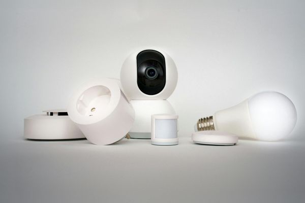 Assorted white smart home devices and light bulbs arranged on a plain white background