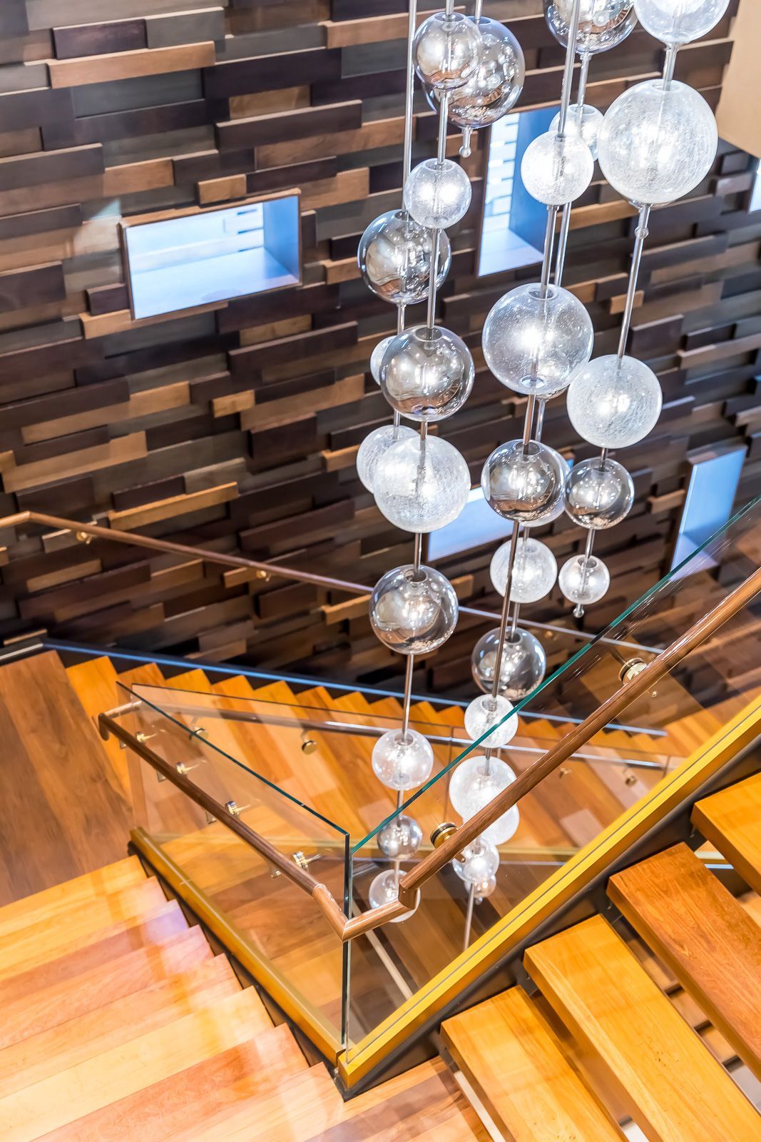 Interior staircase with glass railing and hanging globe chandelier in a modern lobby.