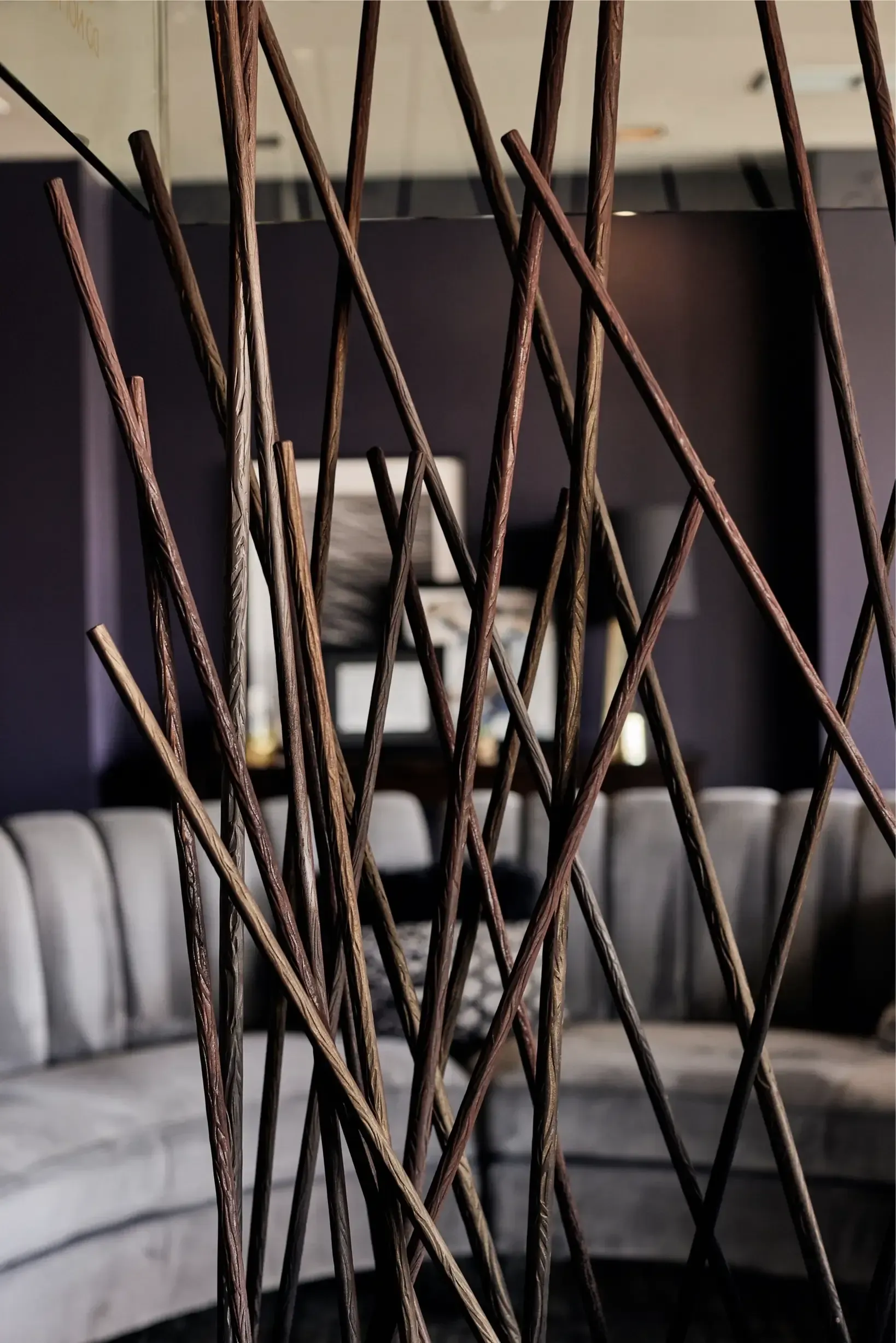 Interior lounge with a sculptural wooden twig divider and gray sectional seating.