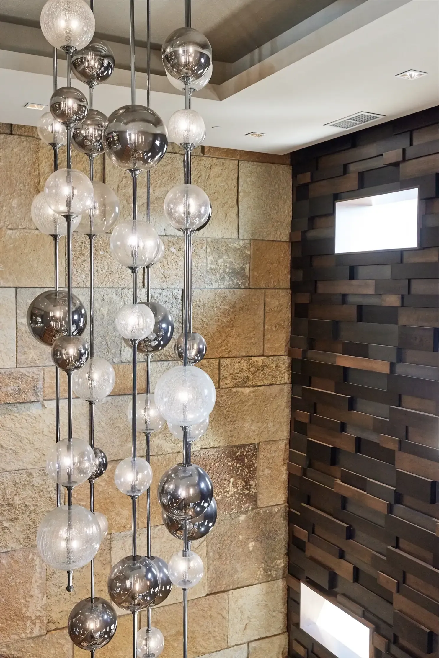 Interior lobby with a chandelier of glass globe orbs against stone and wood walls.