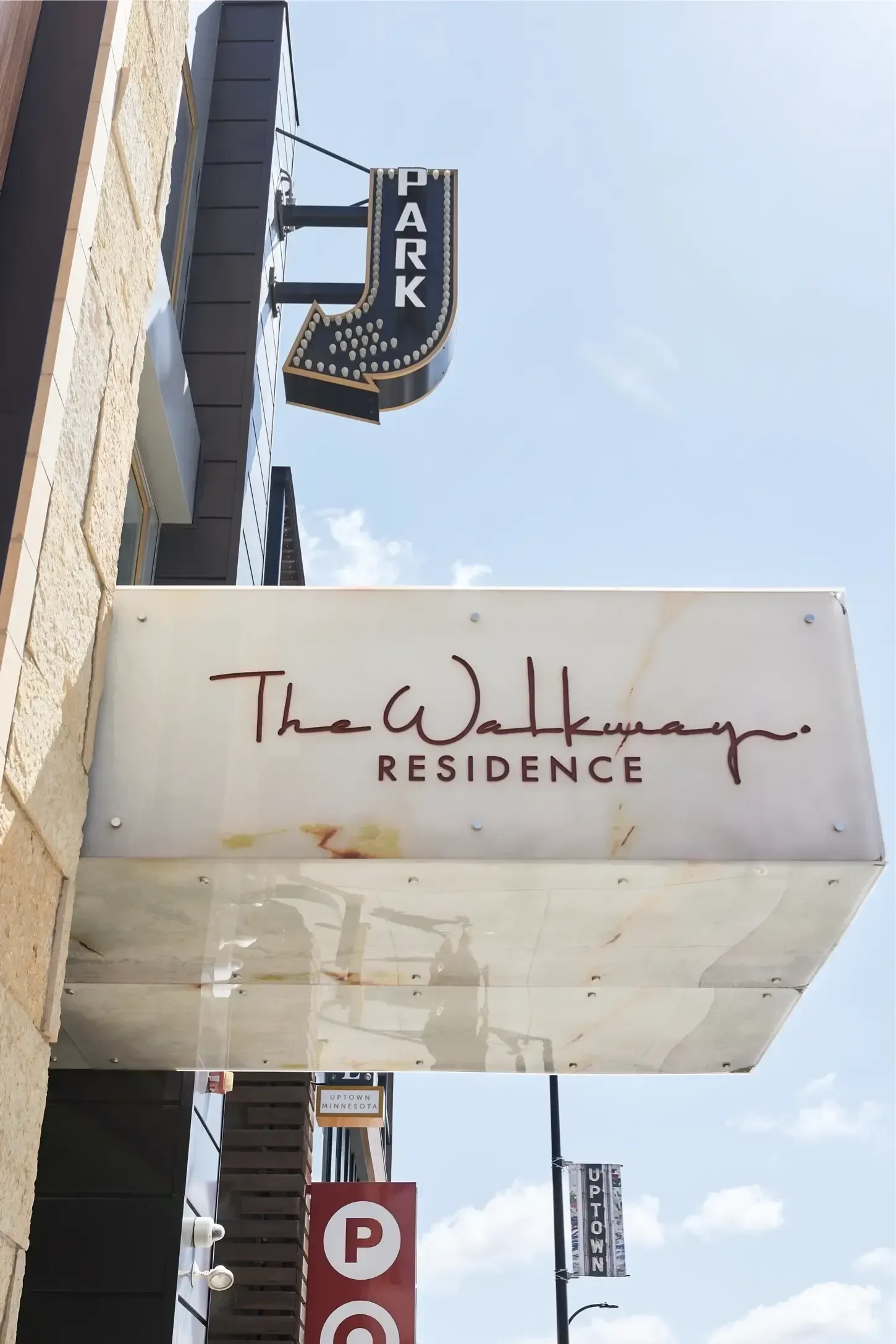 Exterior view of The Walkway Residence sign on a building with a vertical PARK sign and blue sky.