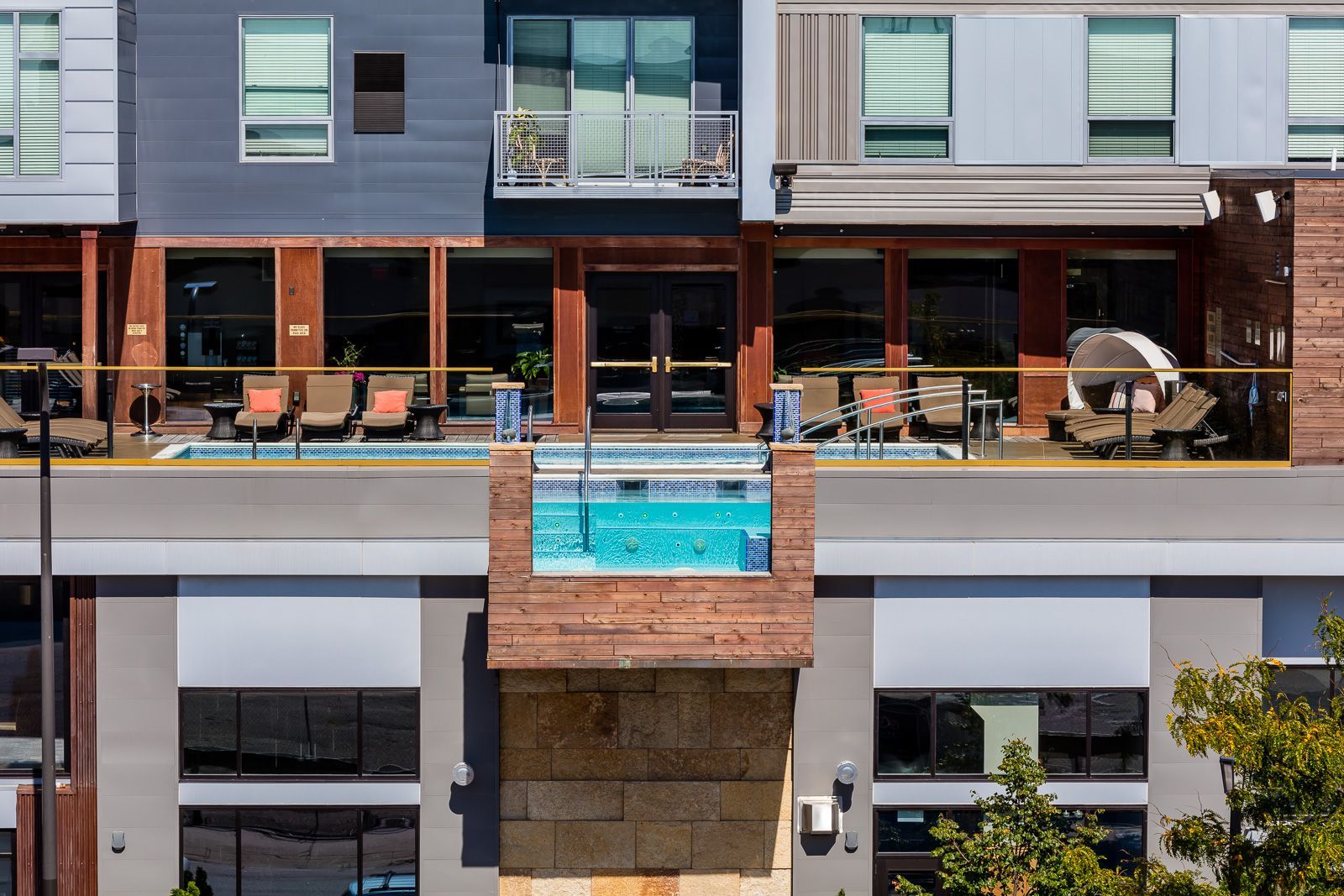 Exterior view of a modern apartment building with an outdoor pool and lounge seating on a deck.