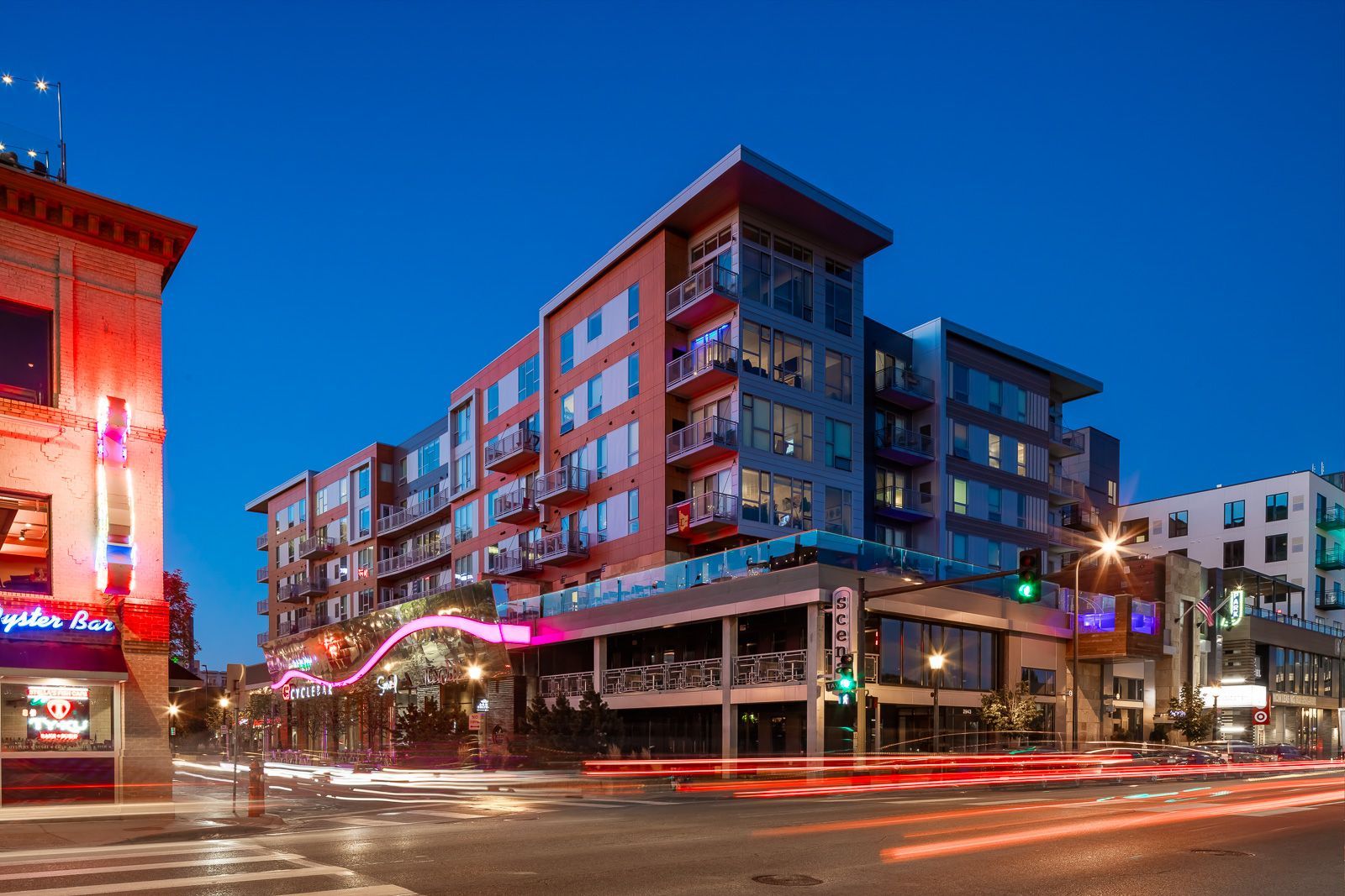 Exterior view of a modern apartment building at dusk with neon signs along the street.