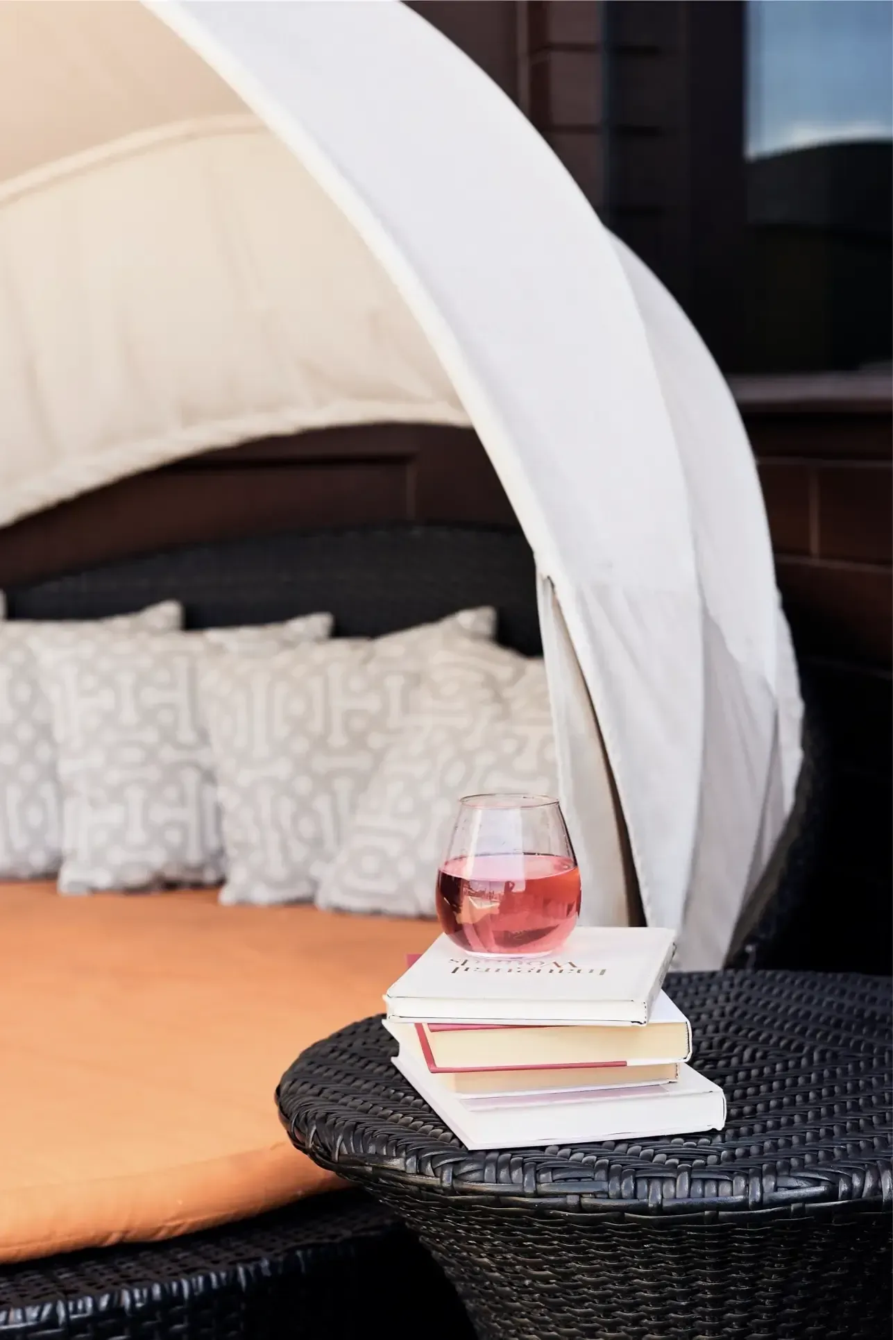 Outdoor community lounge with a white canopy, cushions, and a pink drink on a wicker table.