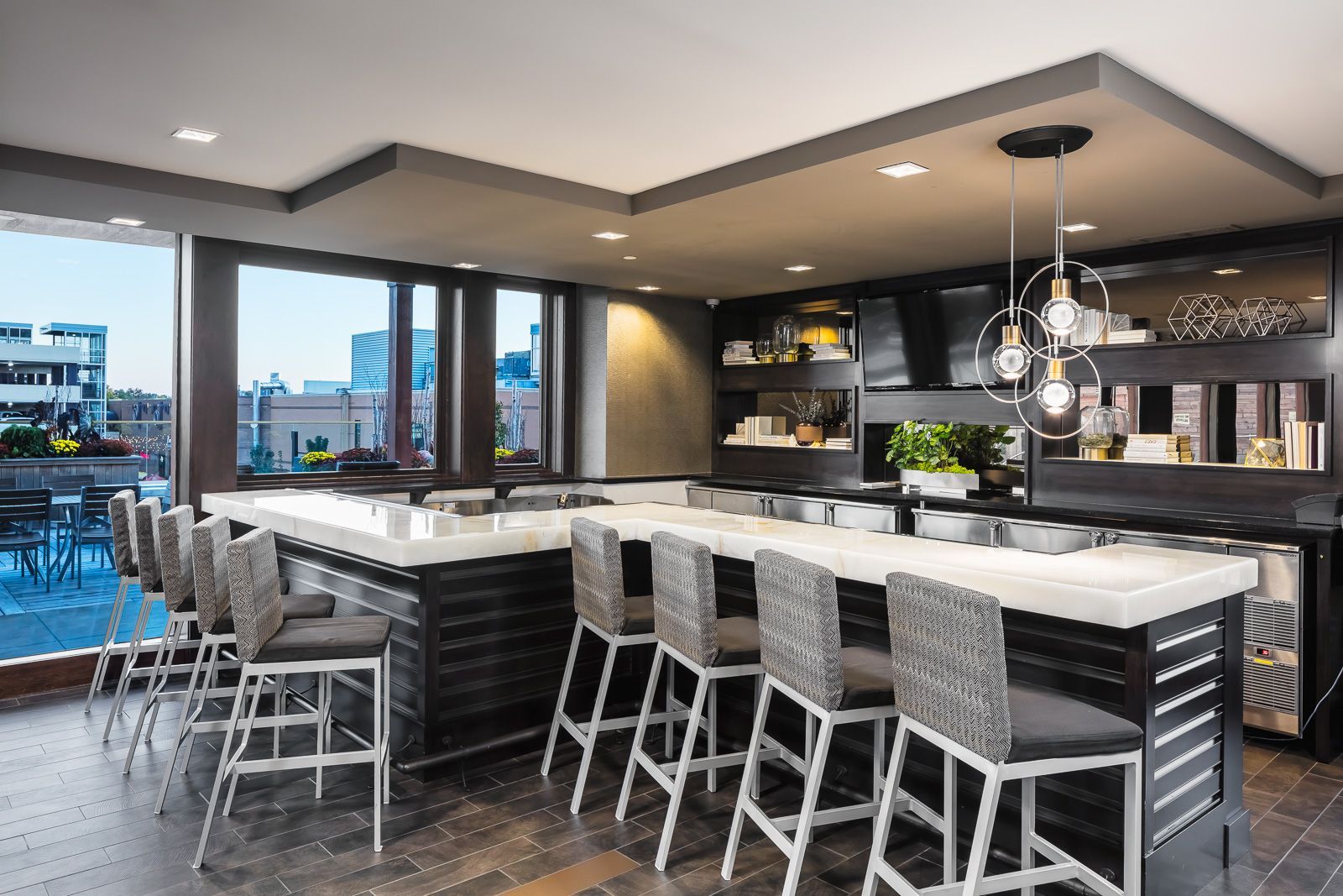 Modern community bar area with a marble-topped island, high chairs, and built-in shelving.