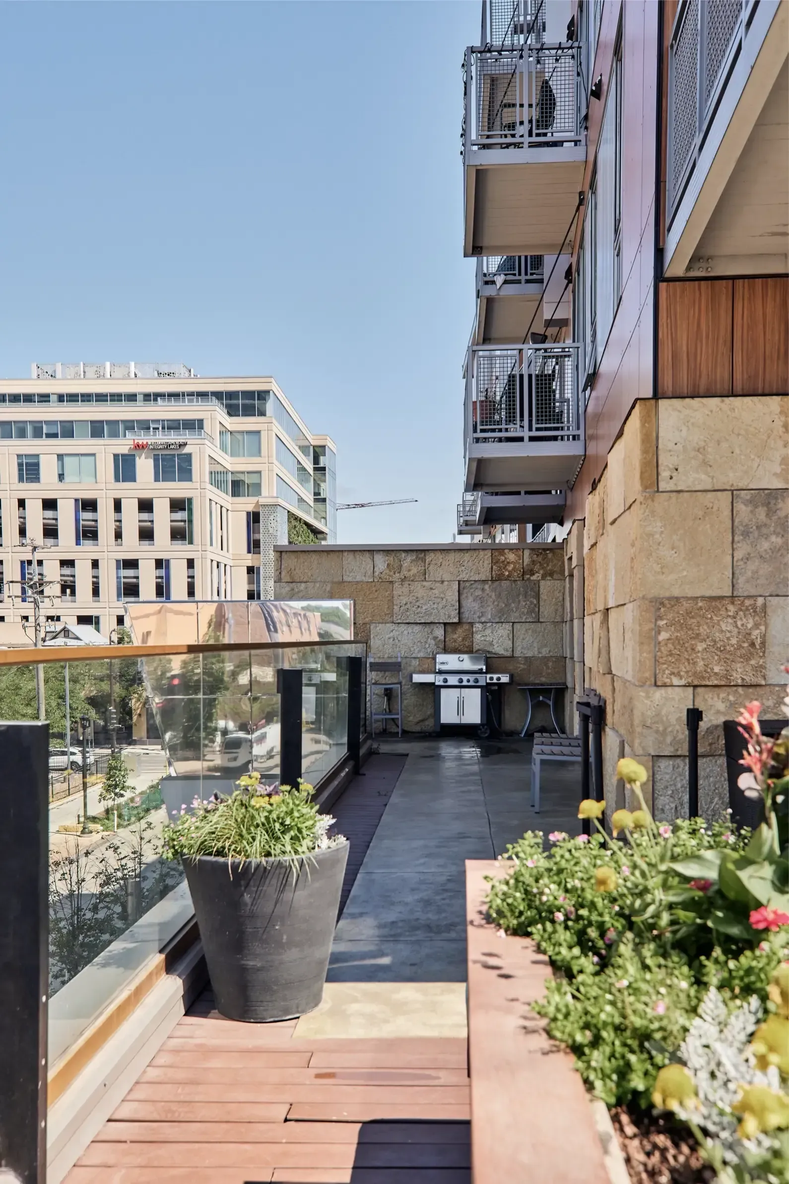 Balcony of an apartment with large planters and a grill, overlooking a city street.
