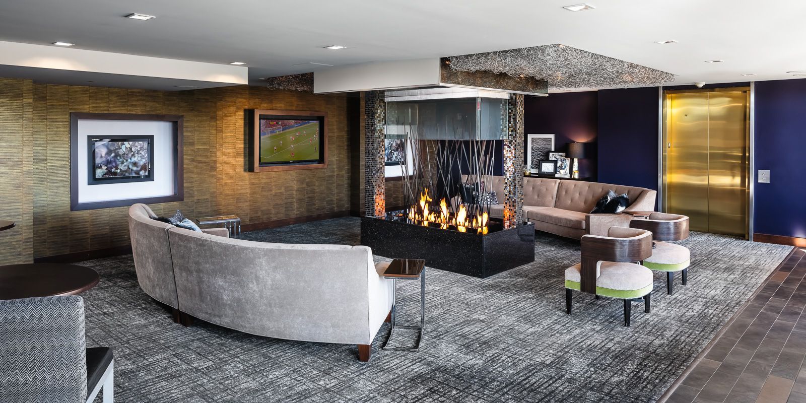 Modern residential lobby with sofas, a glass fireplace, artwork, and an elevator.