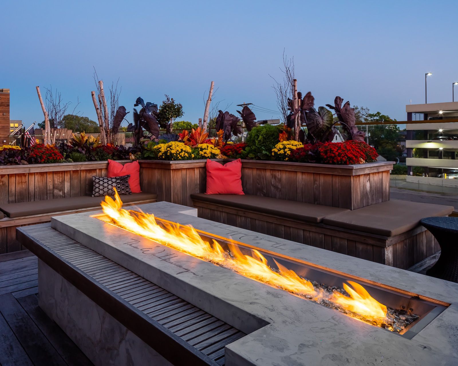 Outdoor rooftop lounge with a long fire pit, built-in benches, and colorful planters.
